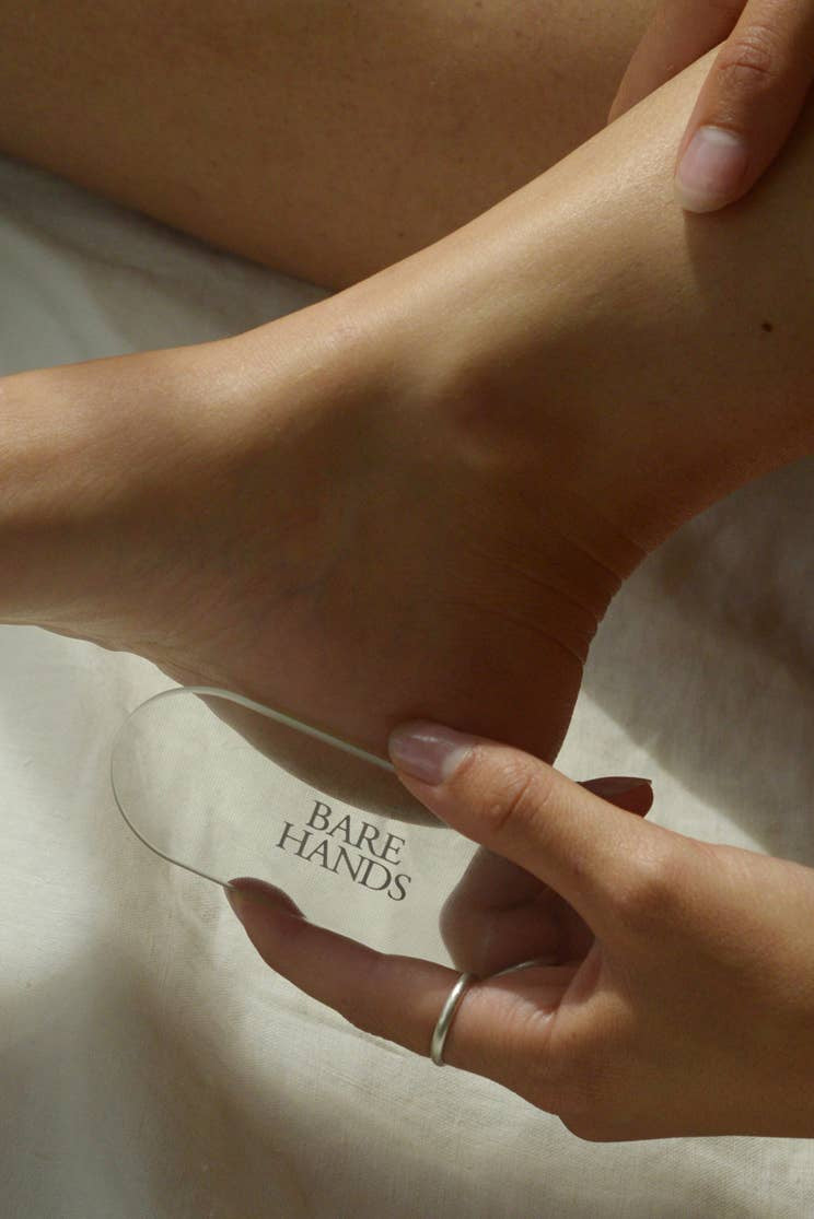 Person holding a glass with 'Bare Hands' branding near their foot.