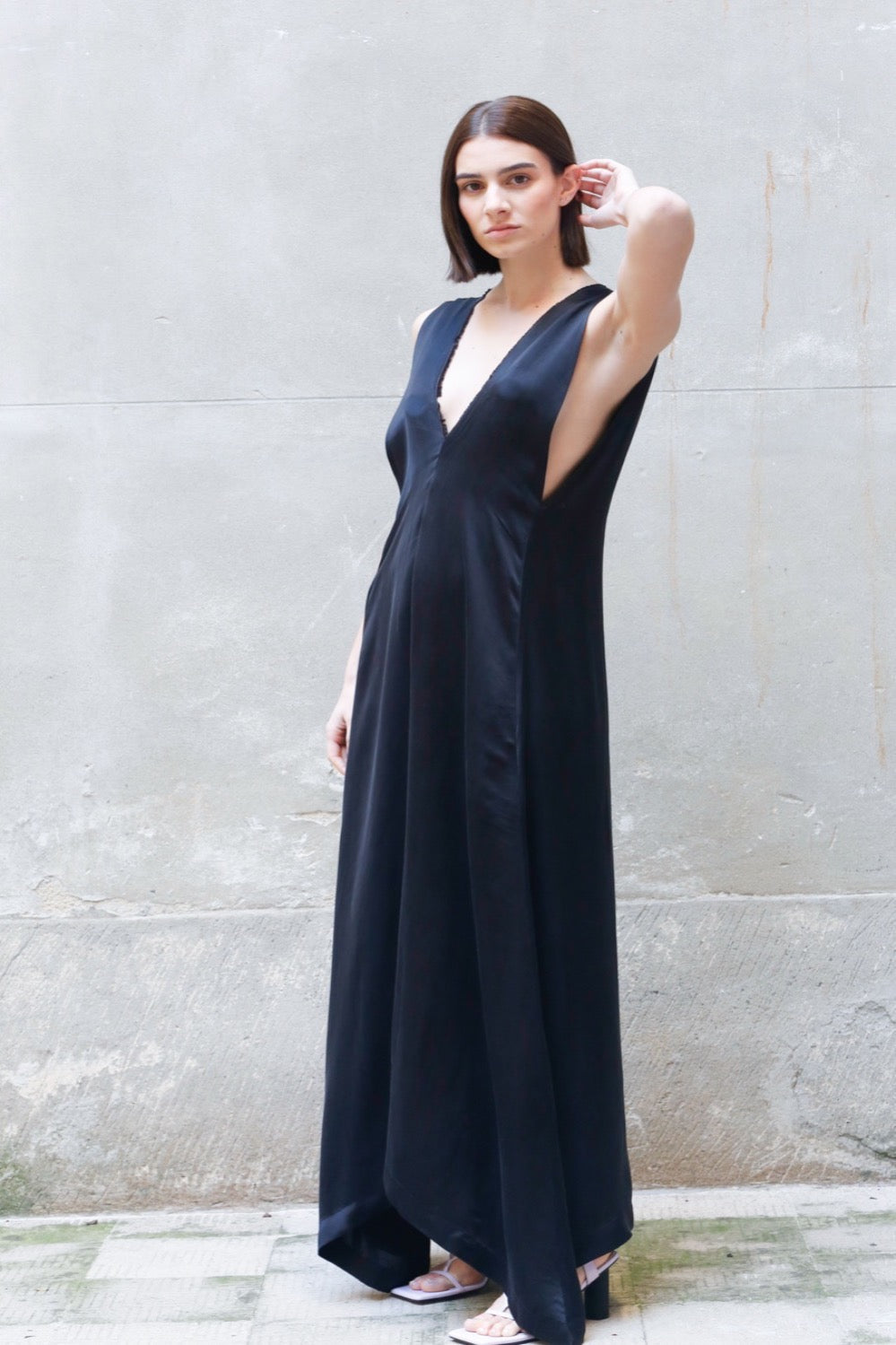 Woman wearing a dark blue sleeveless dress against a light gray wall.