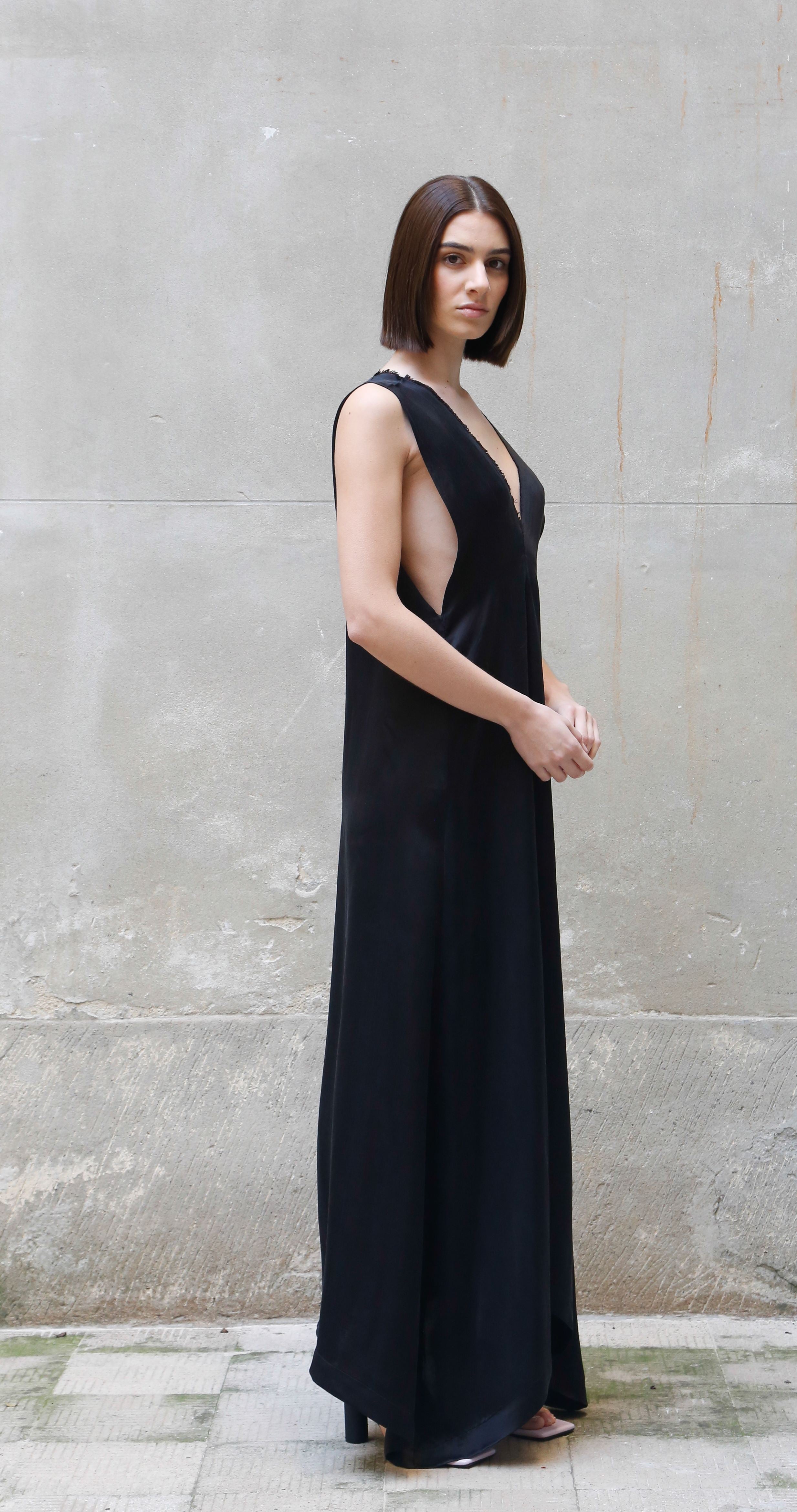 Woman wearing a black dress standing against a gray wall.