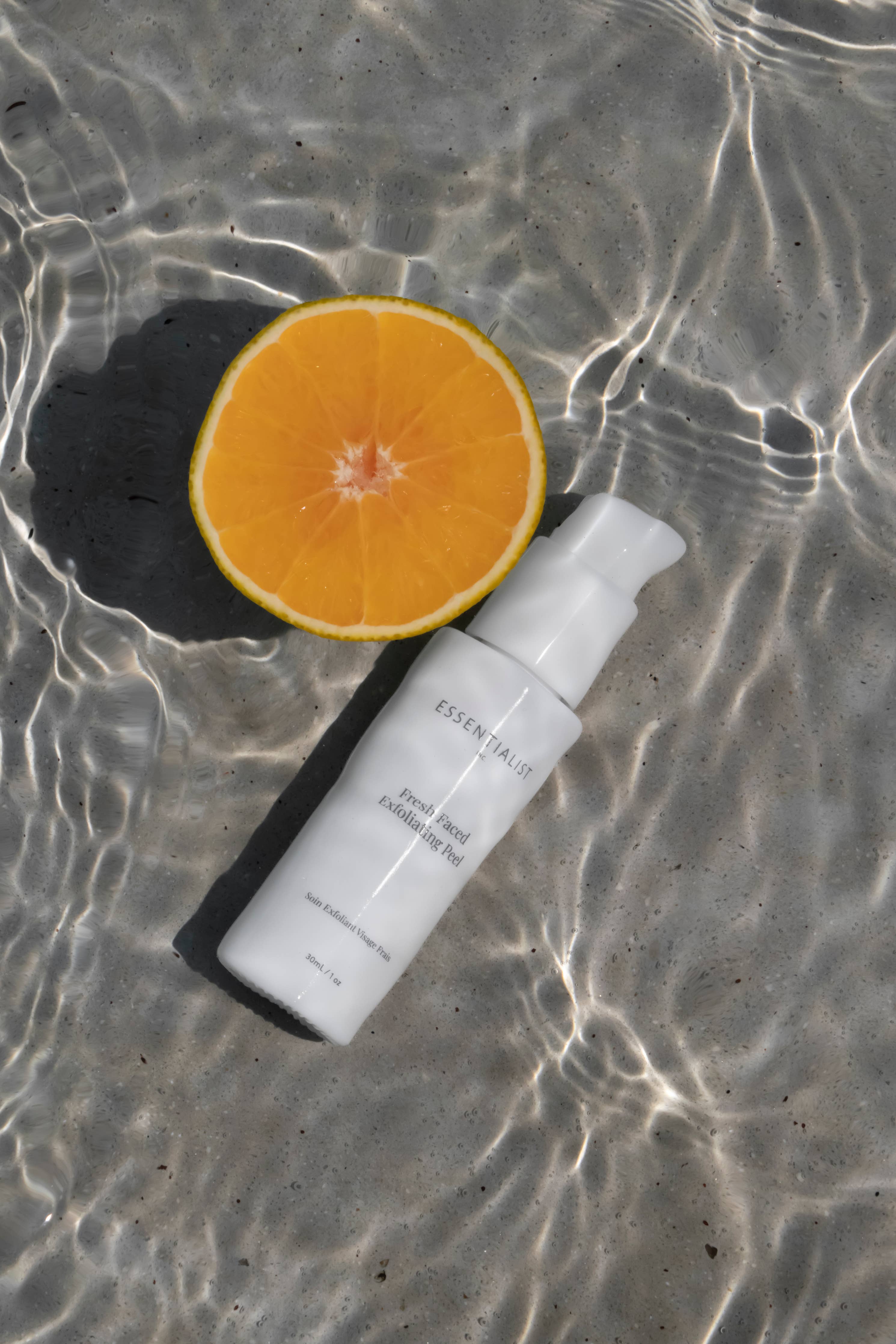 Skincare bottle and sliced orange on wet sand