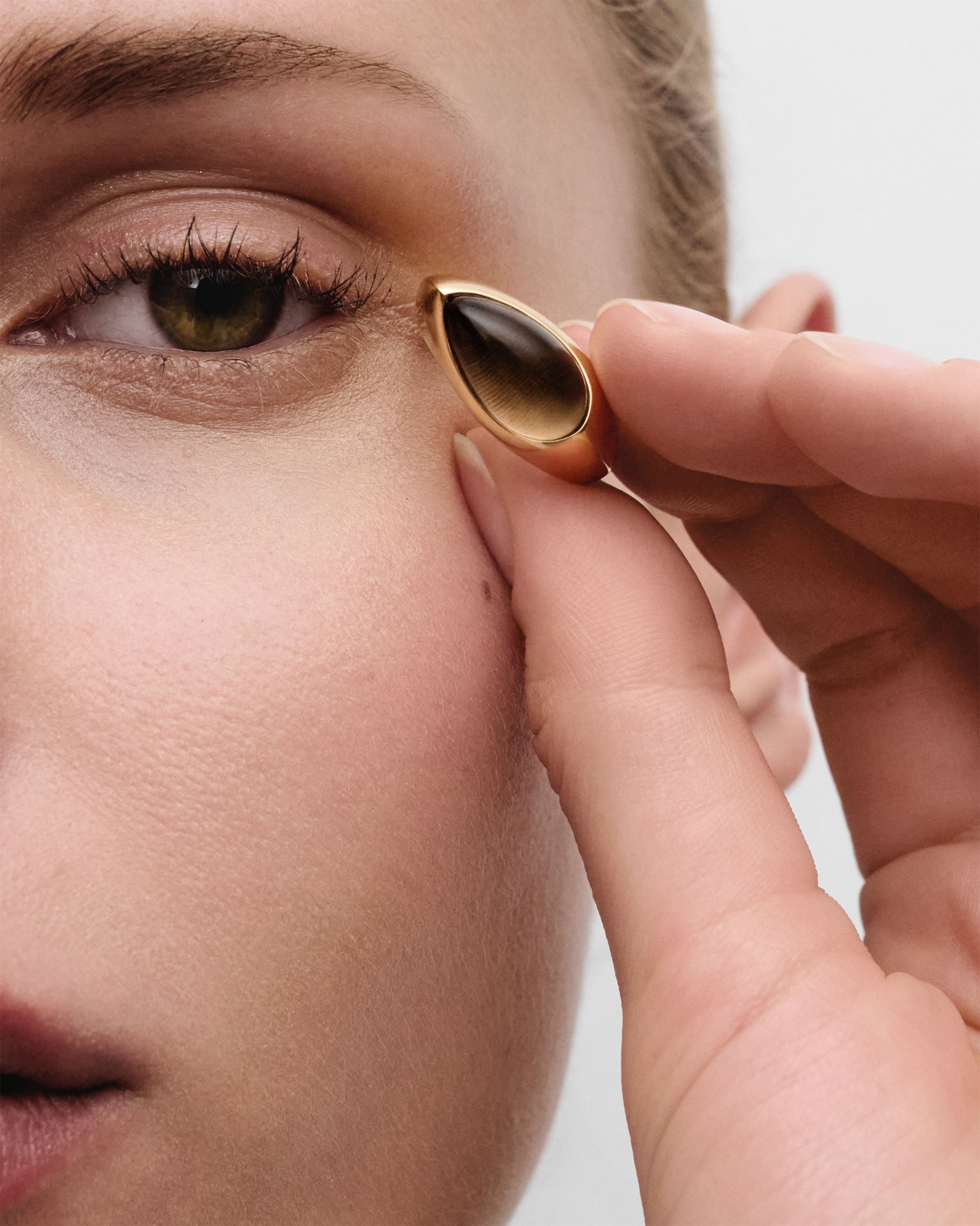 Close-up of a hand holding up a gold ring that has a drop shaped brown quartz gemstone.