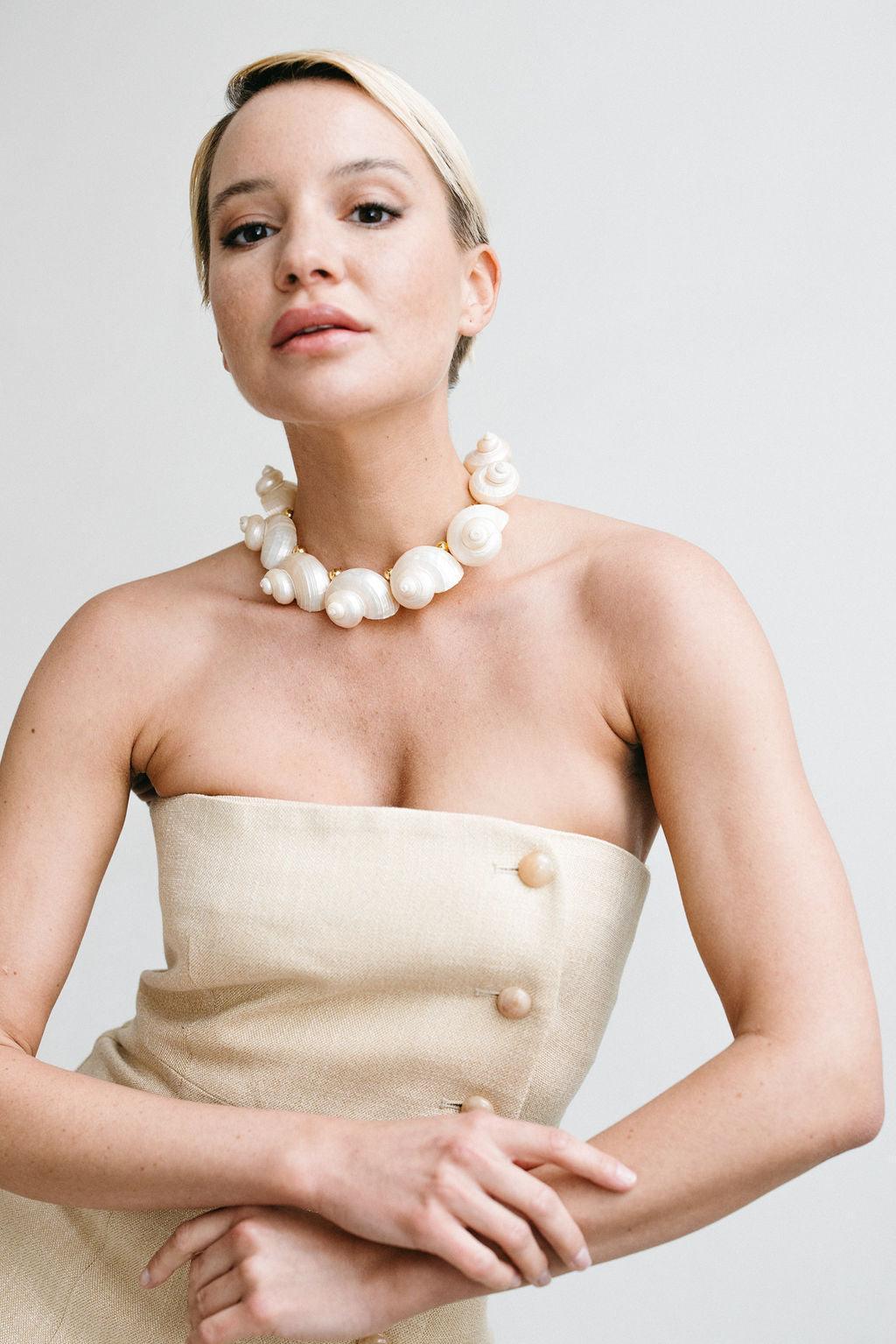Woman wearing a strapless beige dress and pearl necklace against a plain background