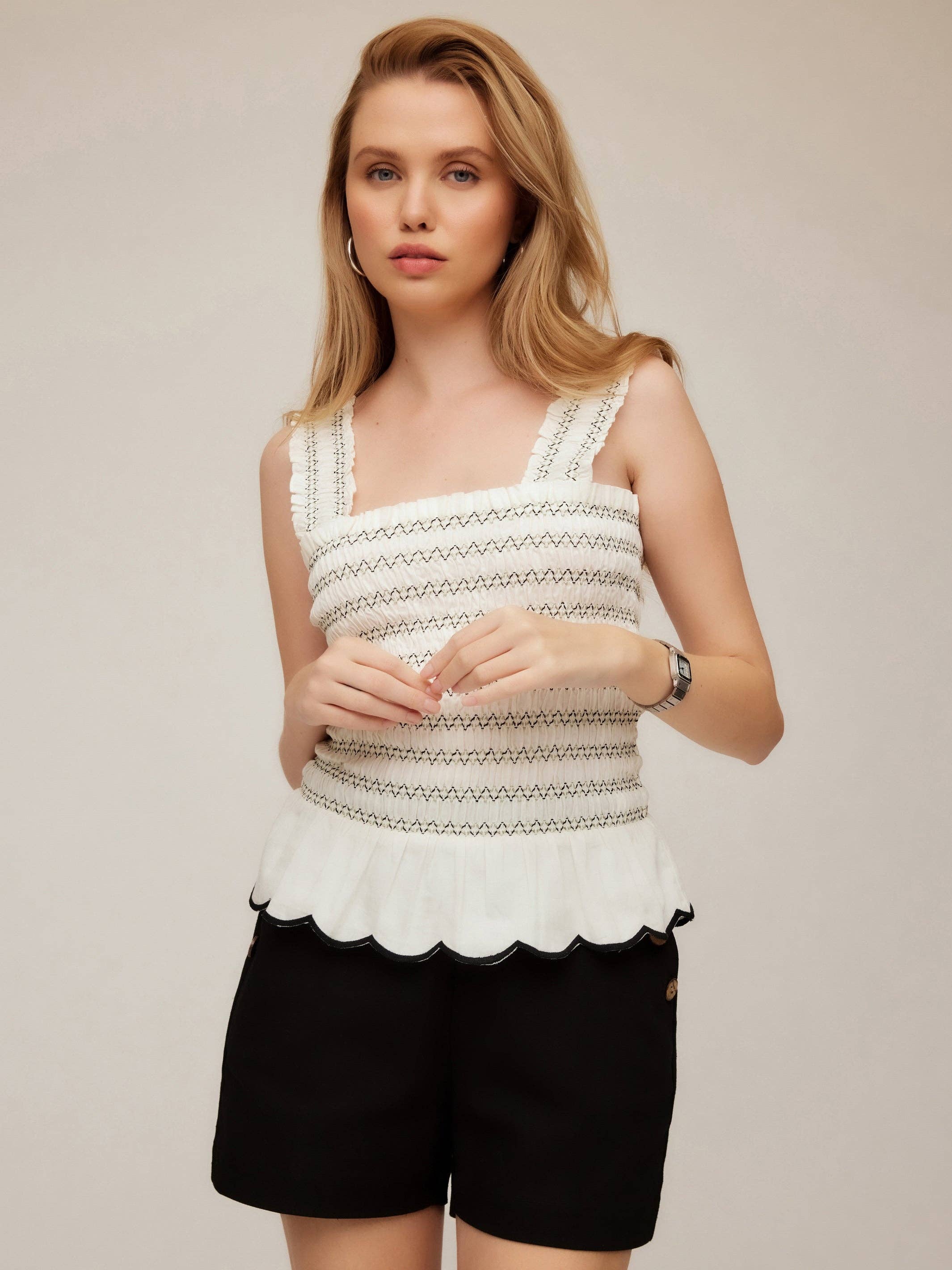 Woman wearing a white sleeveless top with black patterns and black shorts on a beige background