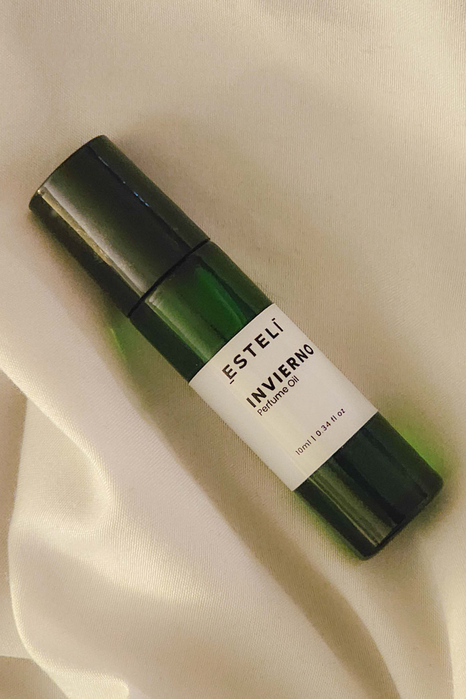 Green Esteli perfume bottle on a beige fabric background