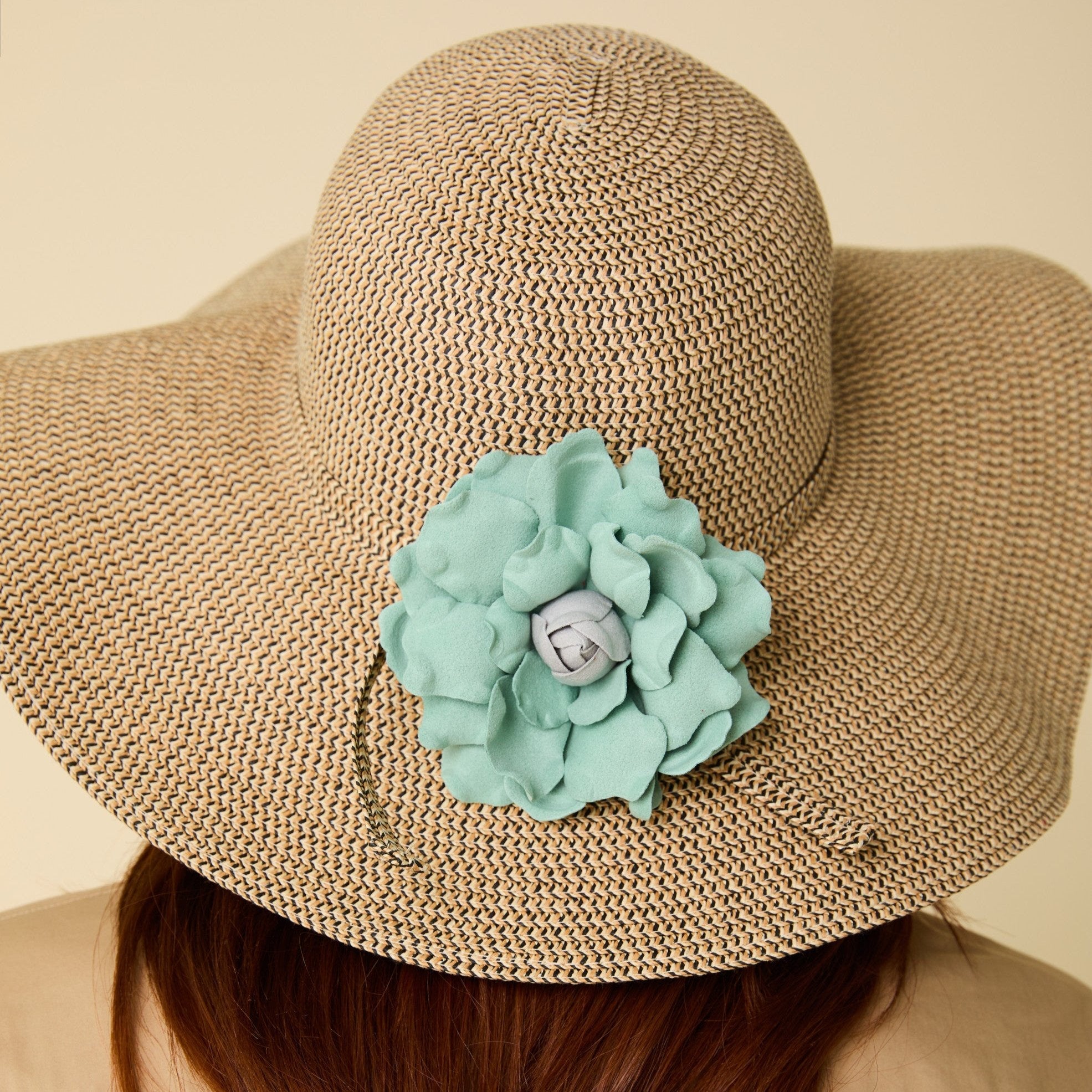Beige straw hat with a large turquoise flower accessory on a beige background