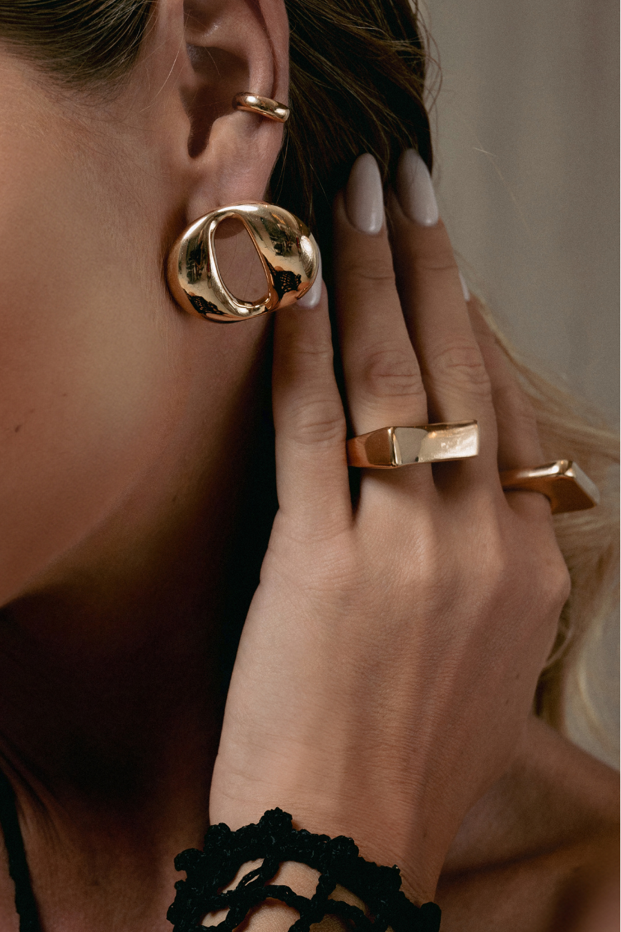 Close-up of a woman wearing gold earrings and rings with a neutral background