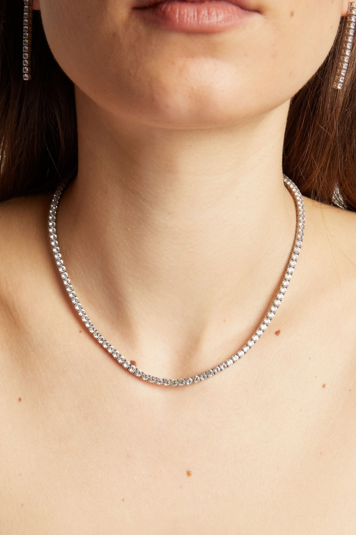 Close-up of a woman wearing a silver necklace and black strappy top against a neutral background
