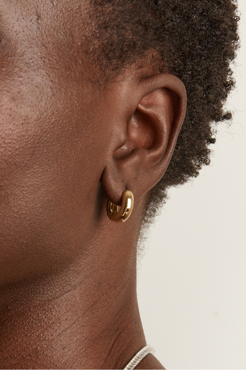 Close-up of a person wearing gold hoop earrings with a neutral background