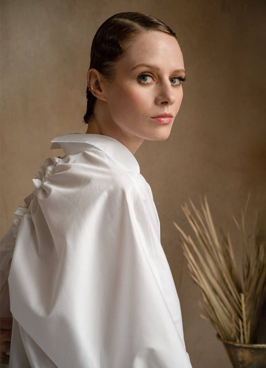 Woman wearing a white garment with ruffled sleeves against a neutral background