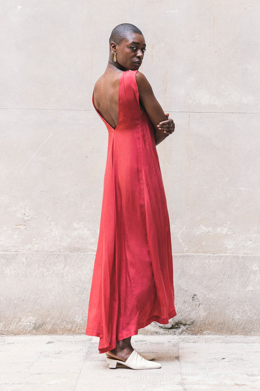Woman in a red dress standing against a light-colored wall.