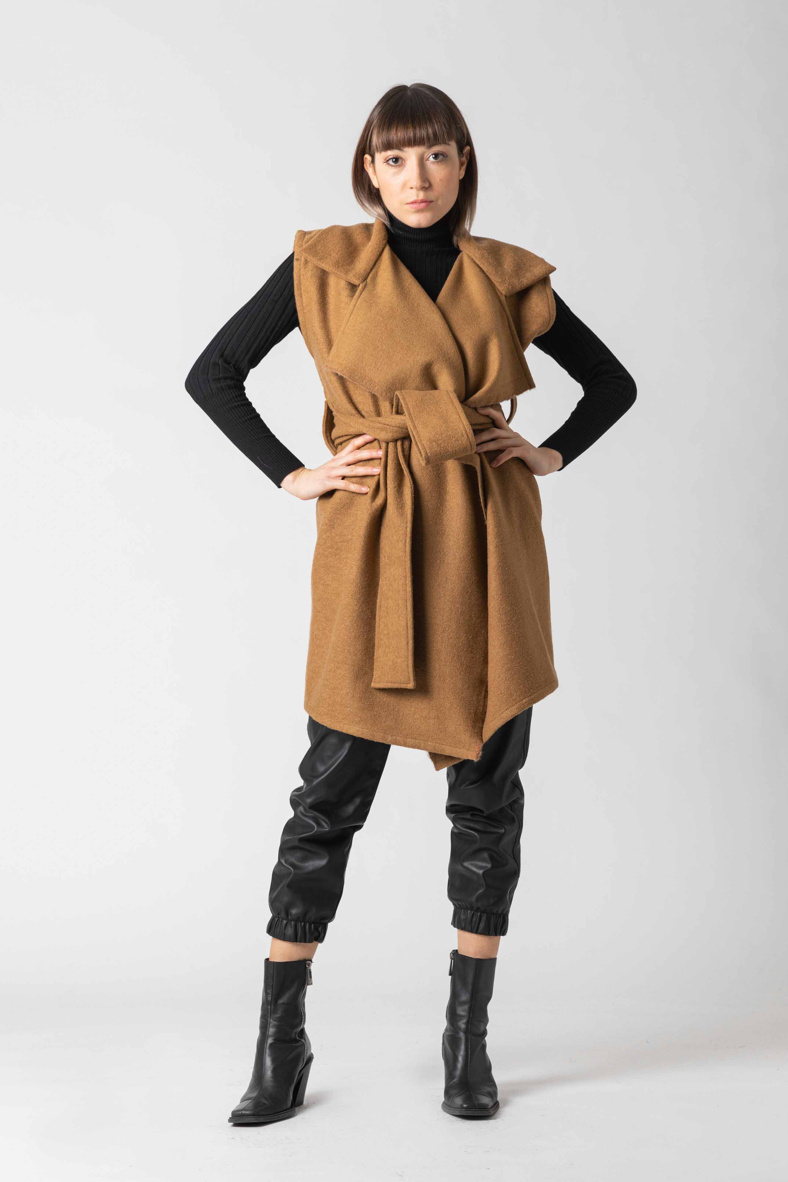 Woman wearing a brown vest over a black top and pants on a white background