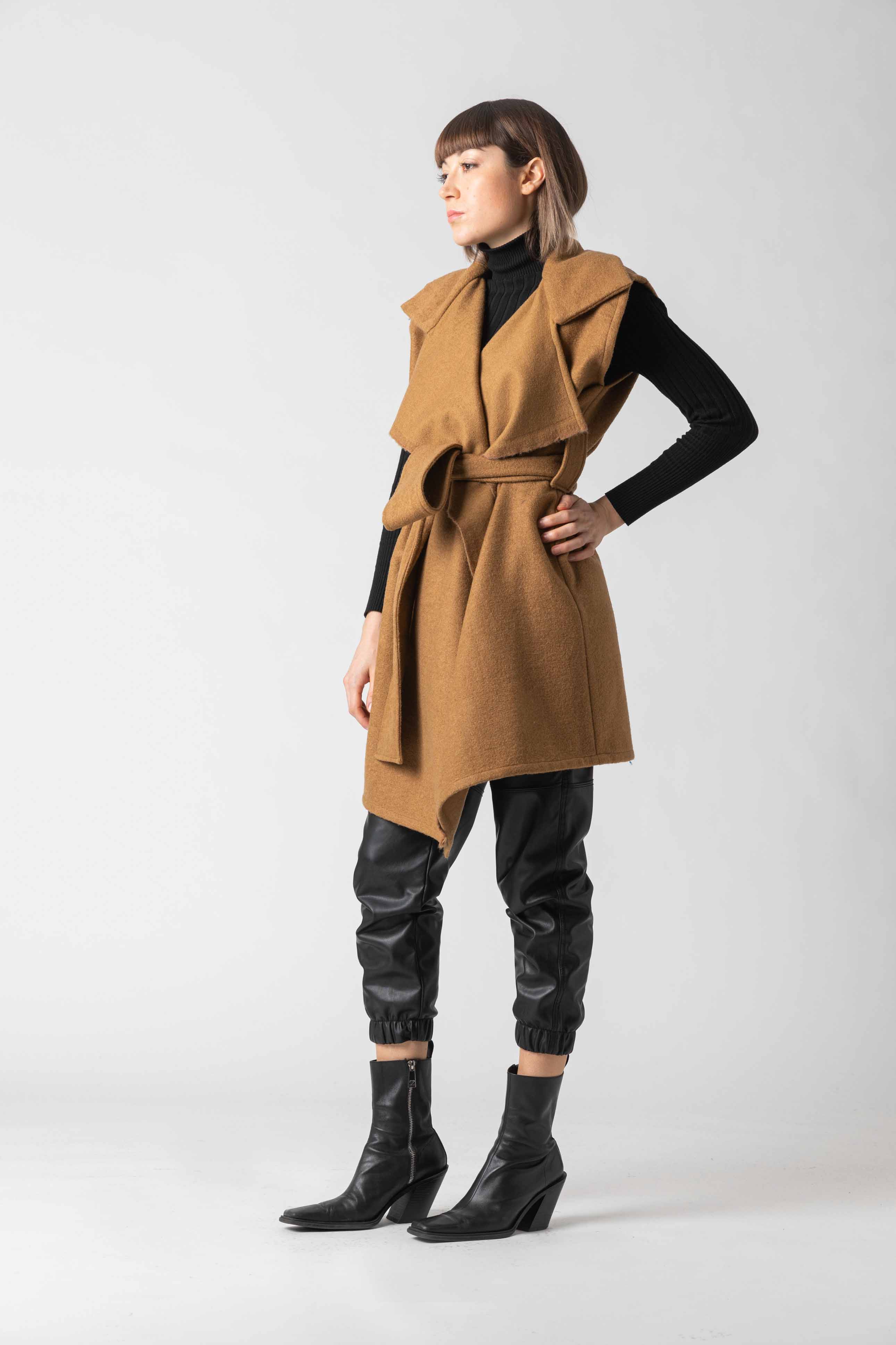 Woman wearing a tan vest over a black outfit on a white background