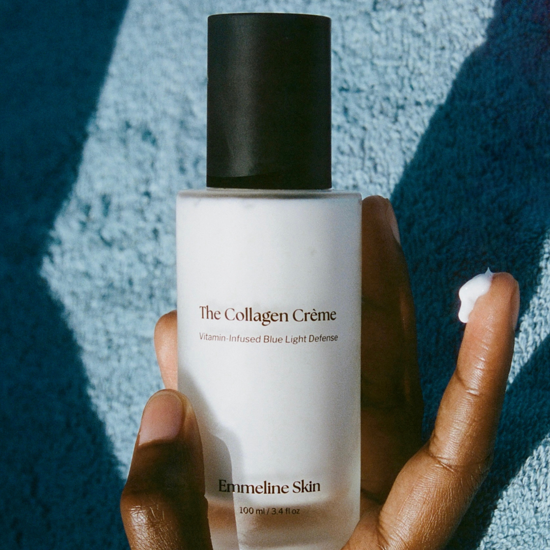 Hand holding a bottle of 'The Collagen Crème' by Emmeline Skin against a textured blue background
