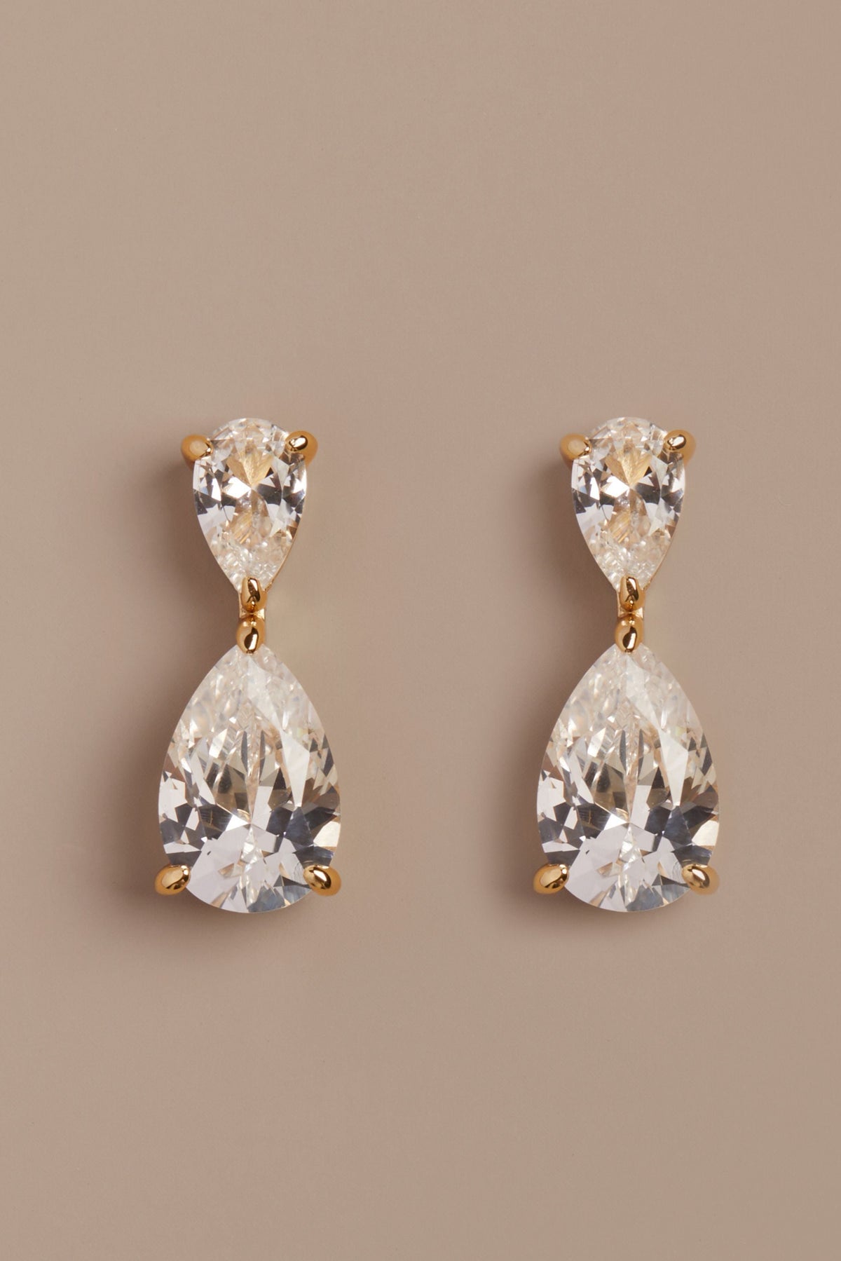 Pair of teardrop-shaped crystal earrings on a beige background