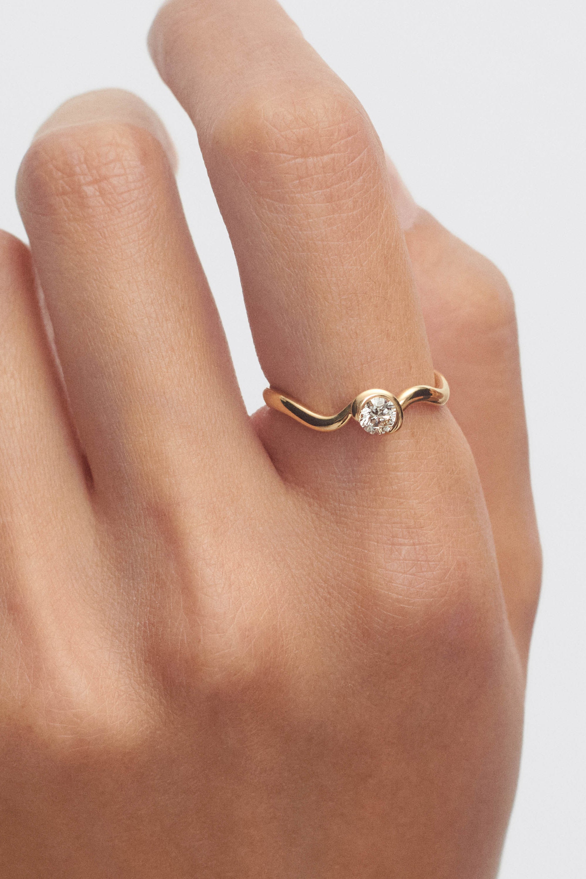 Gold ring with a diamond on a person's finger against a light background