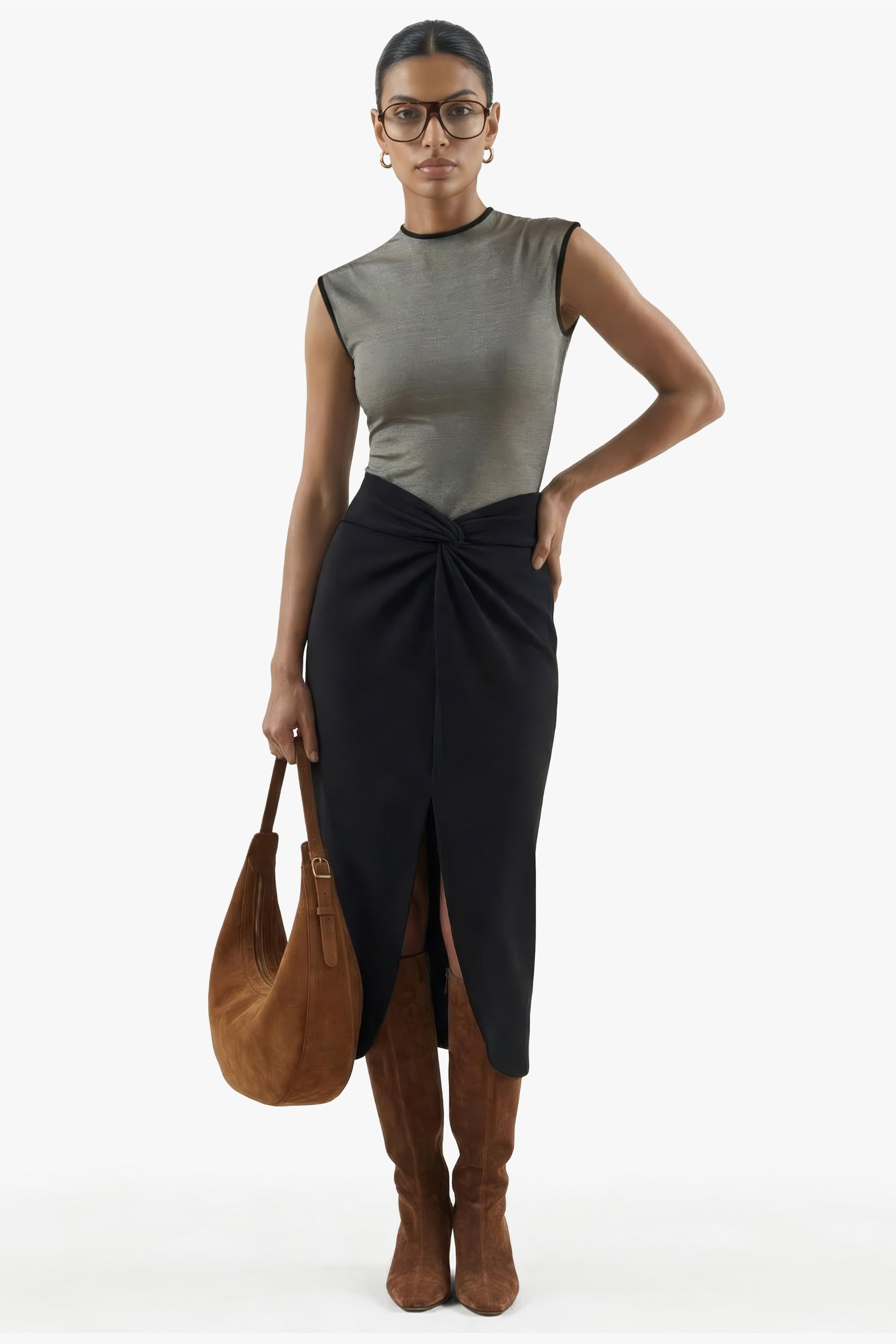 Woman wearing a sleeveless top and black skirt with brown boots and bag on a white background