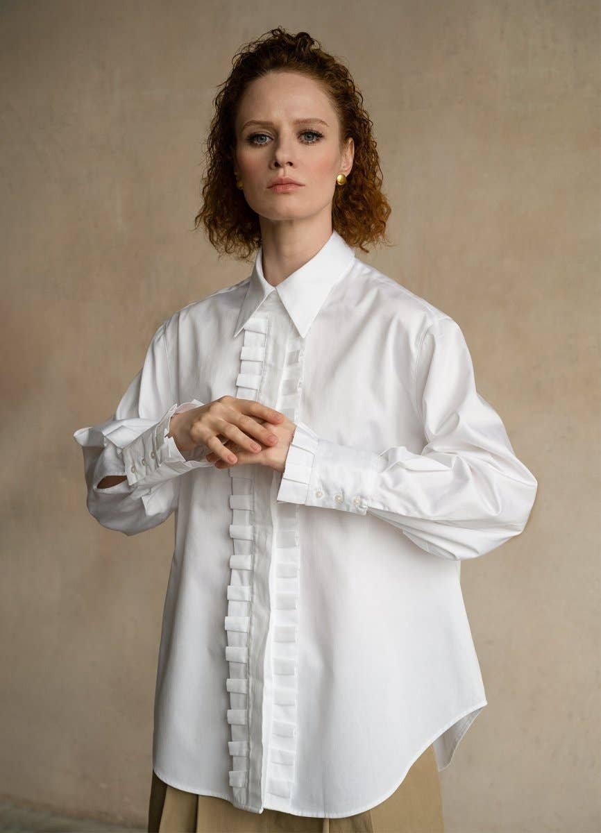 Woman wearing a white blouse with ruffled details against a beige background