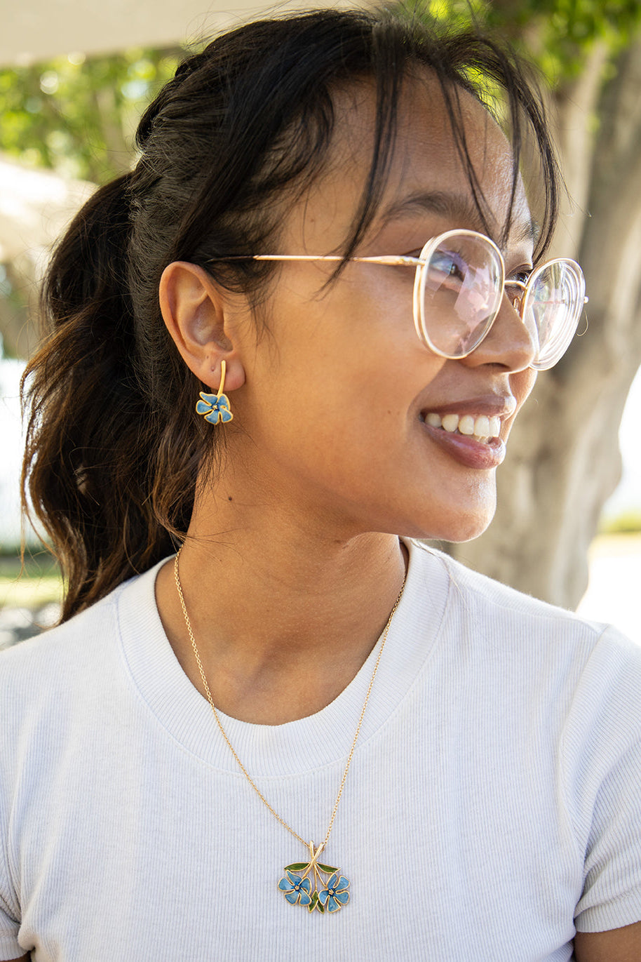 Woman wearing round glasses and a necklace with a pendant outdoors