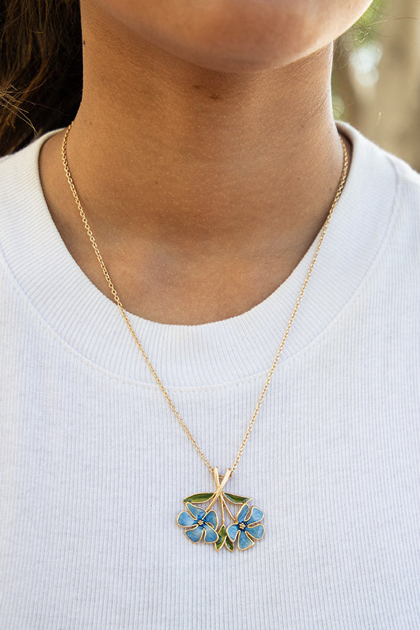 Person wearing a necklace with a floral pendant outdoors