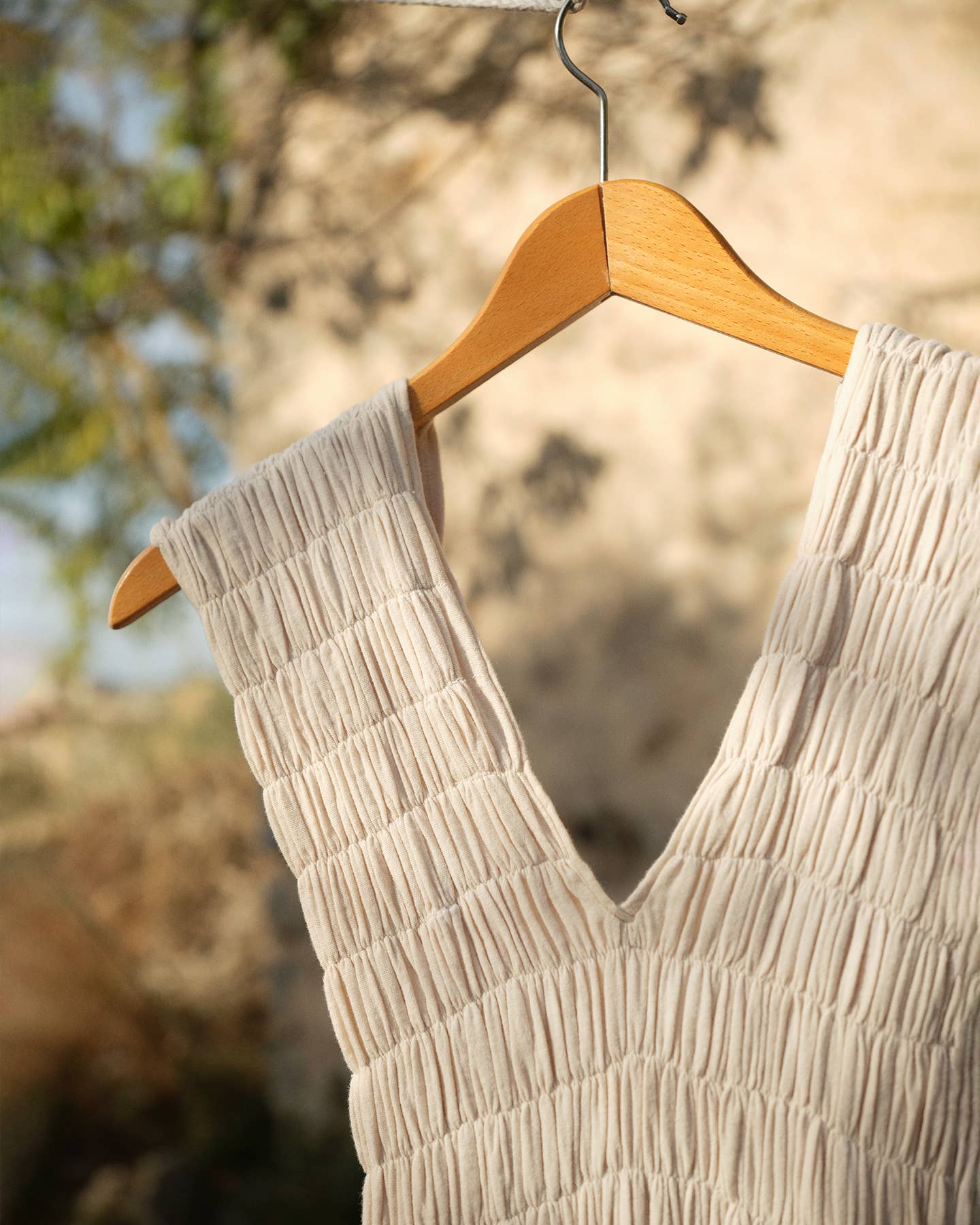 Beige textured dress on a wooden hanger against a blurred natural background