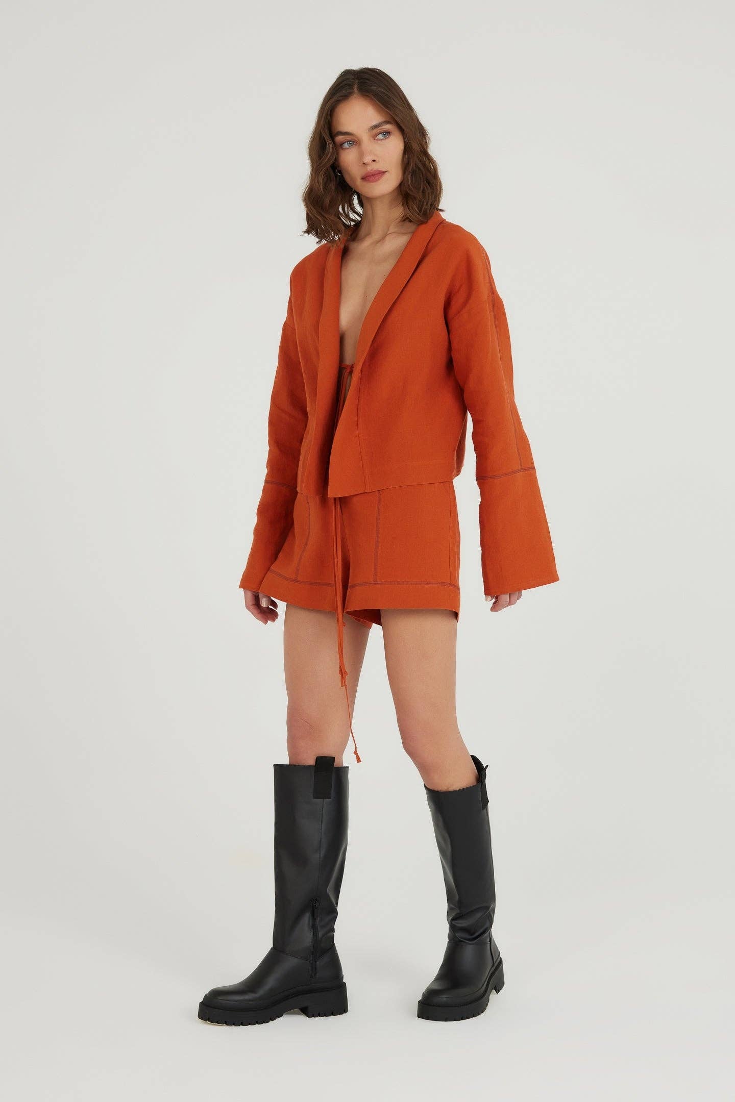 Woman wearing an orange coat and black boots on a white background
