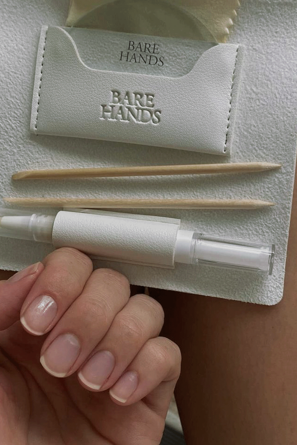 Nail care kit with tools and a pen on a 'Bare Hands' branded paper, held by a hand.