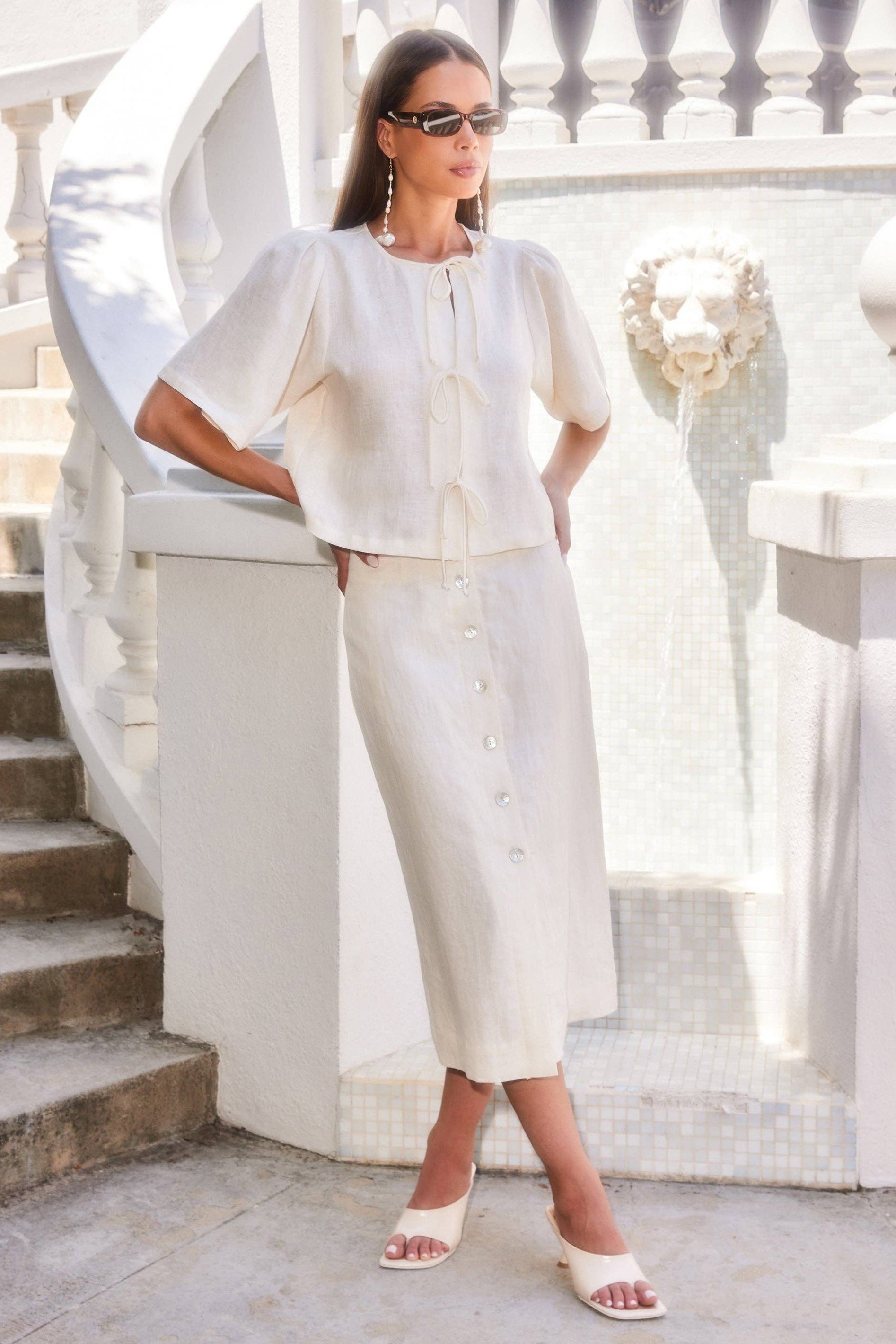 Woman in a white outfit standing on a staircase with decorative railings.