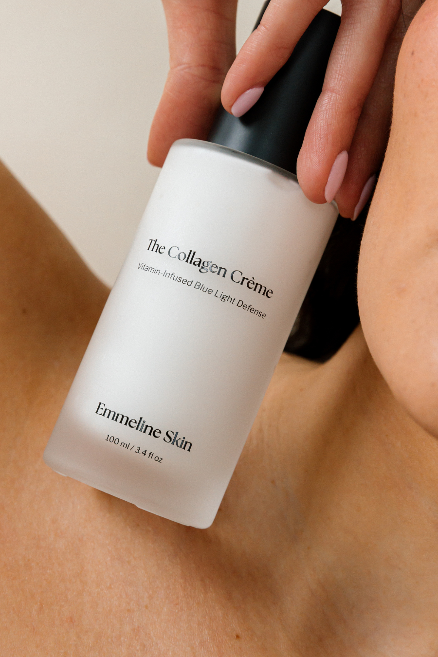 Hand holding a bottle of 'The Collagen Crème' by Emmeline Skin against a neutral background.