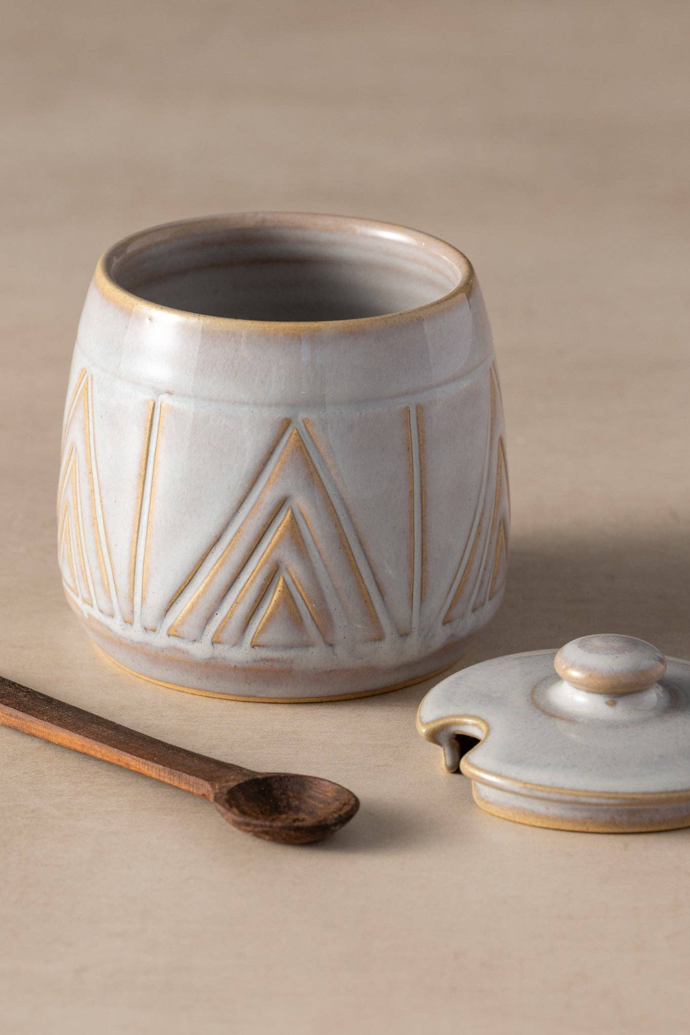 Ceramic jar with lid and wooden spoon on a beige background