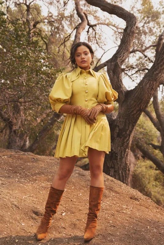 Woman in a yellow dress and brown boots standing in a forest setting