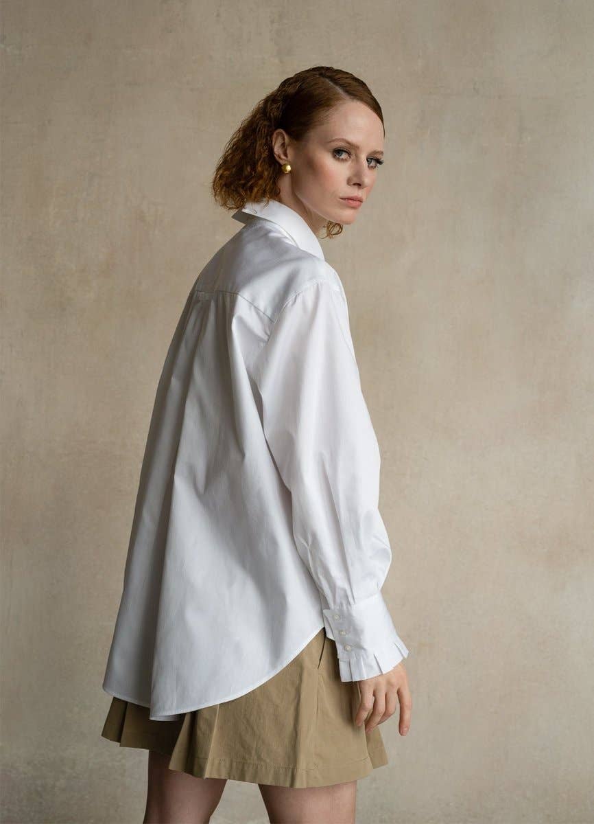 Woman wearing a white shirt and beige skirt against a plain background