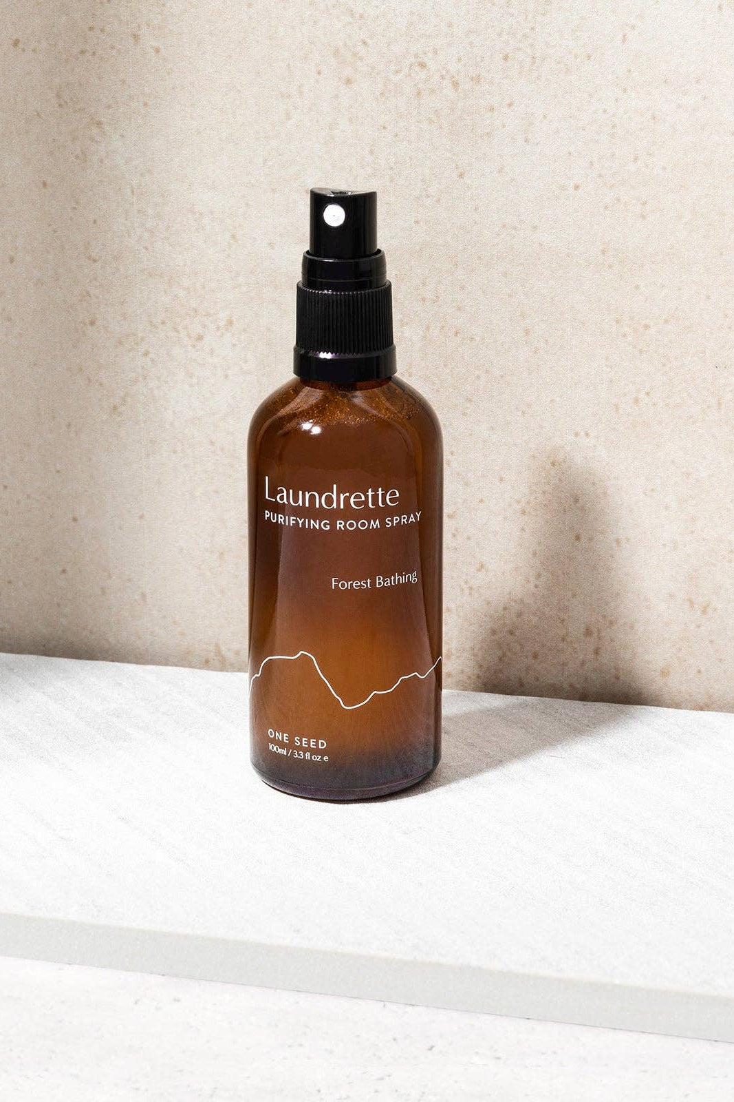 Brown spray bottle labeled 'Laundrette' on a white surface with a beige wall background