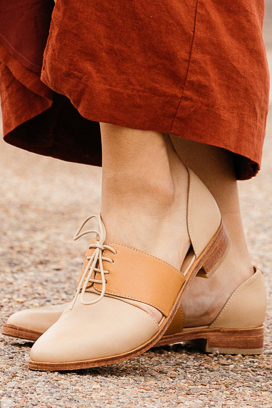 Beige and brown shoes worn with orange pants on a blurred outdoor background