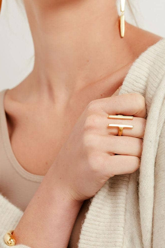 Close-up of a person wearing a gold ring and earring, holding a beige sweater.