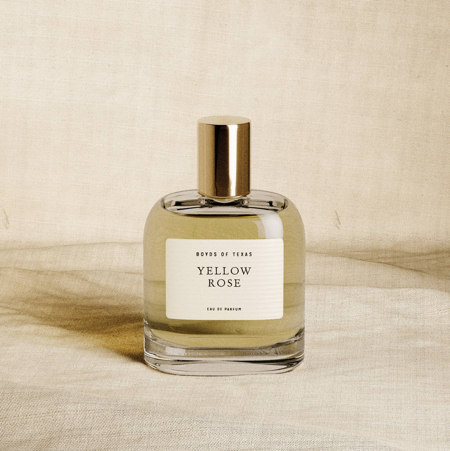 Perfume bottle labeled 'Yellow Rose' by 'Boyds of Texas' on a beige fabric background