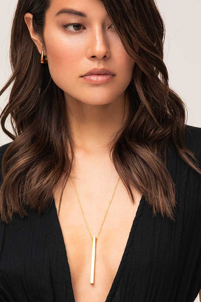 Woman wearing a black top and gold necklace with a plain background