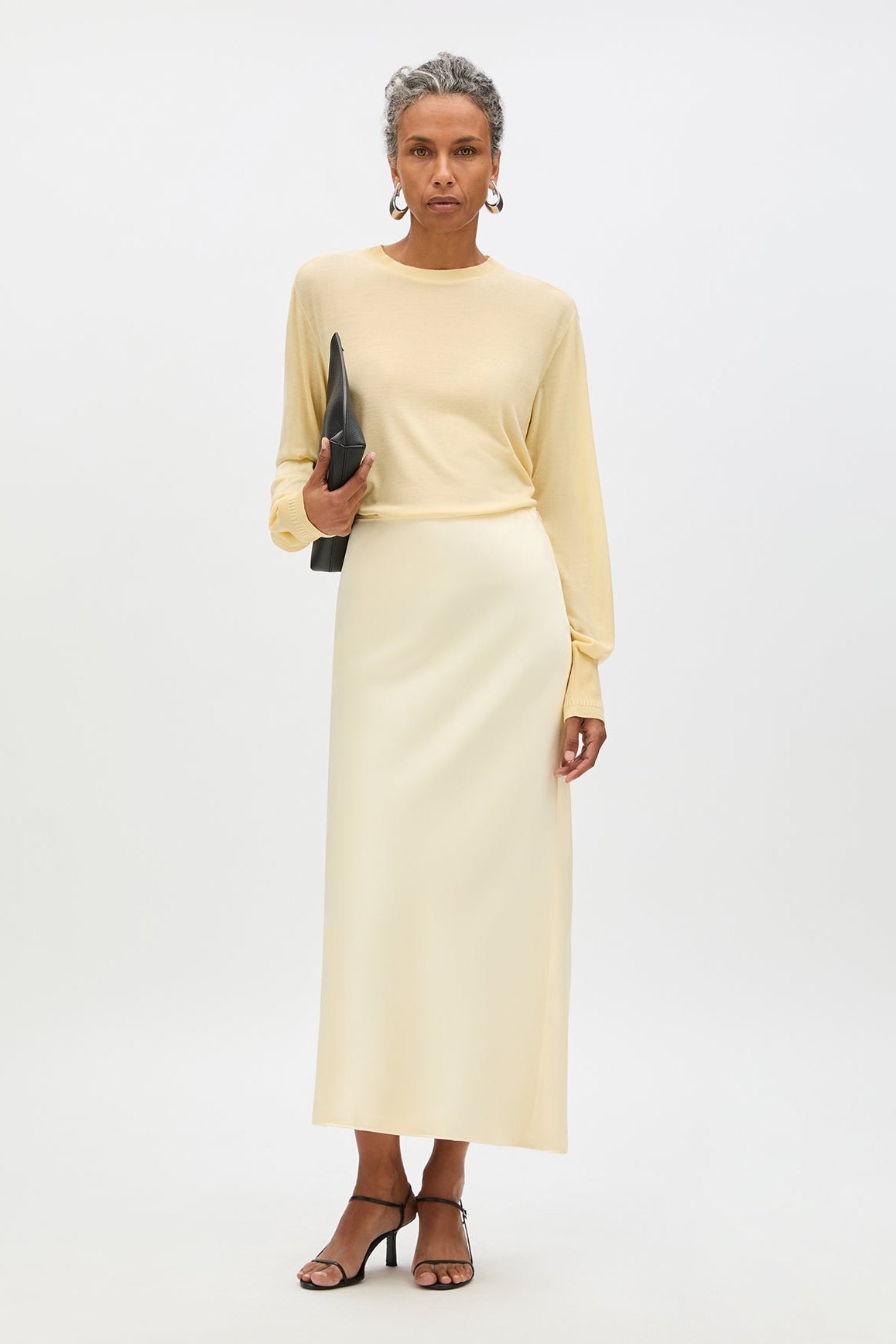 Woman wearing a light yellow dress holding a clutch against a white background