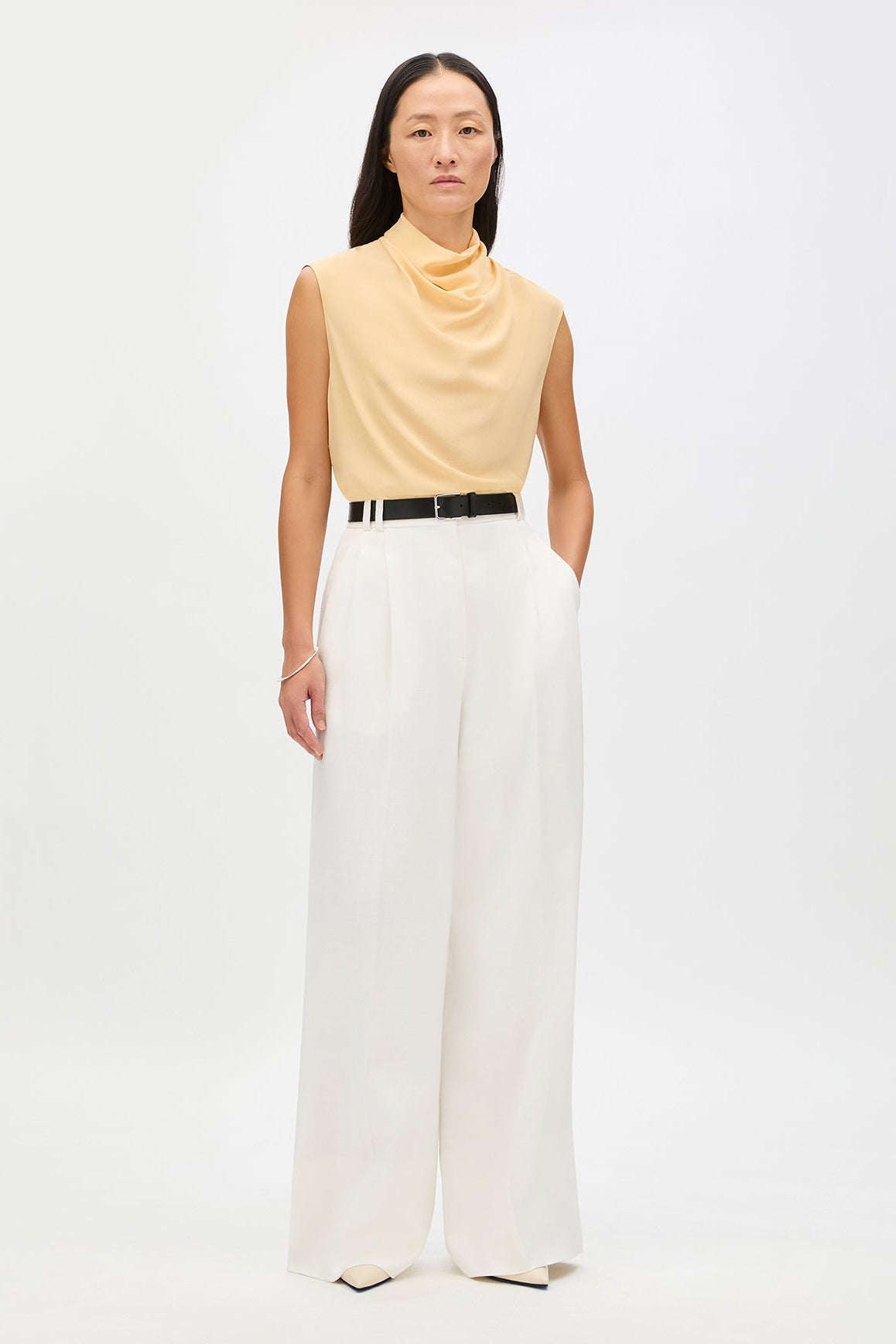 Woman wearing a yellow sleeveless top and white pants on a white background