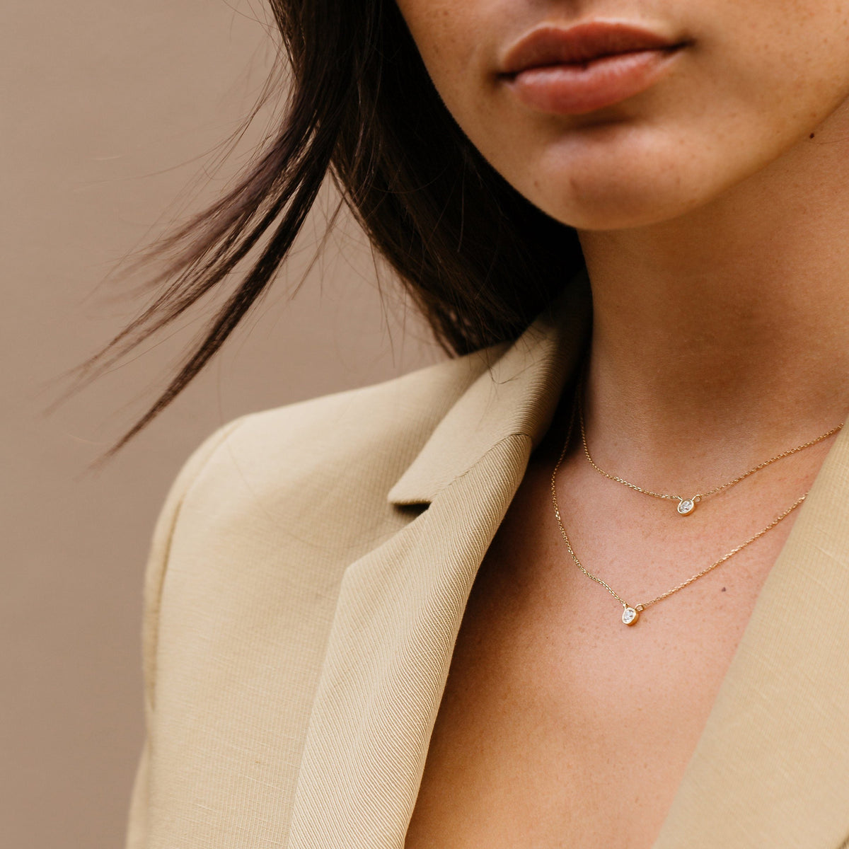 Close-up of a woman wearing a gold necklace with a beige background