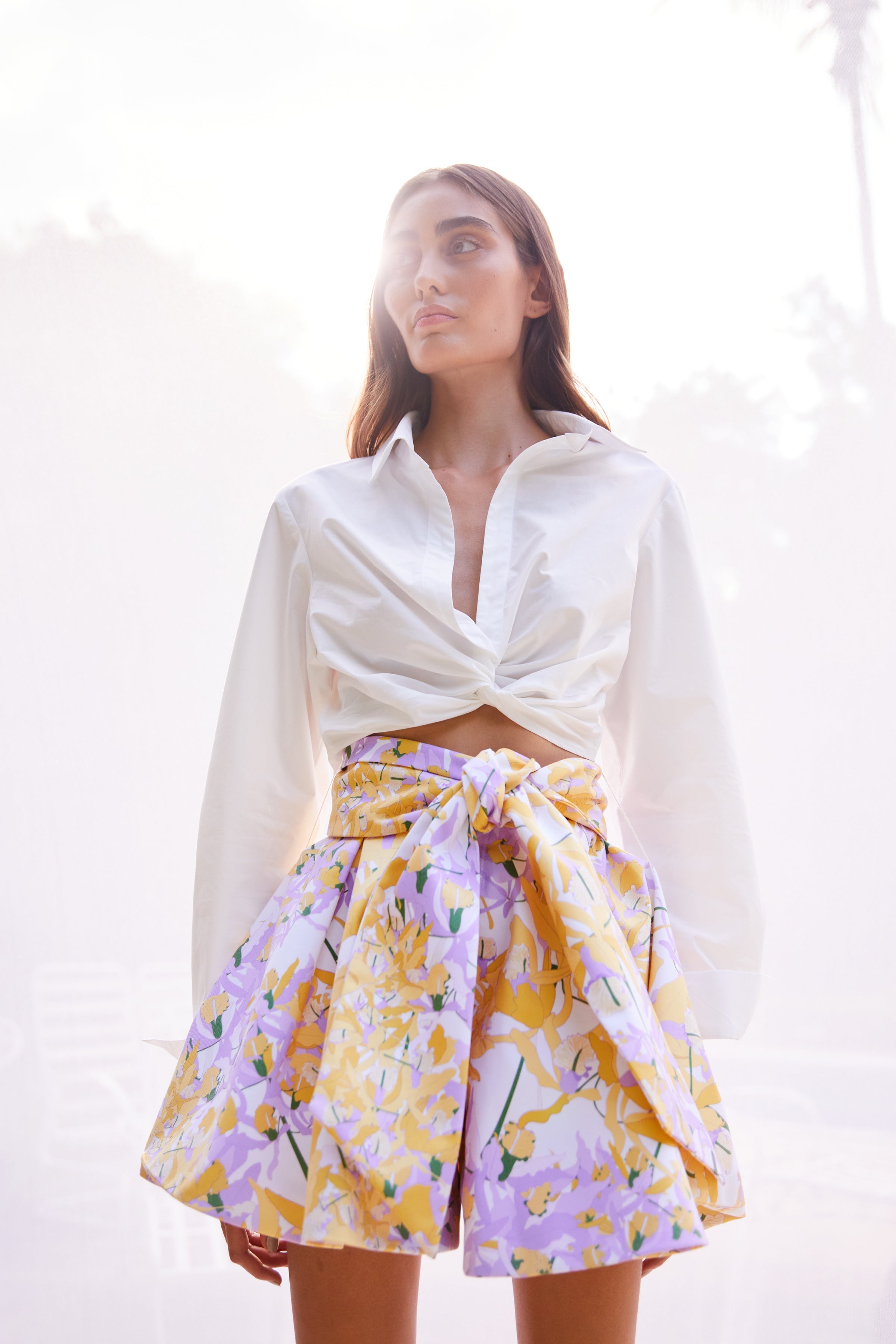 Woman wearing a white cropped blouse and a colorful floral skirt against a white background