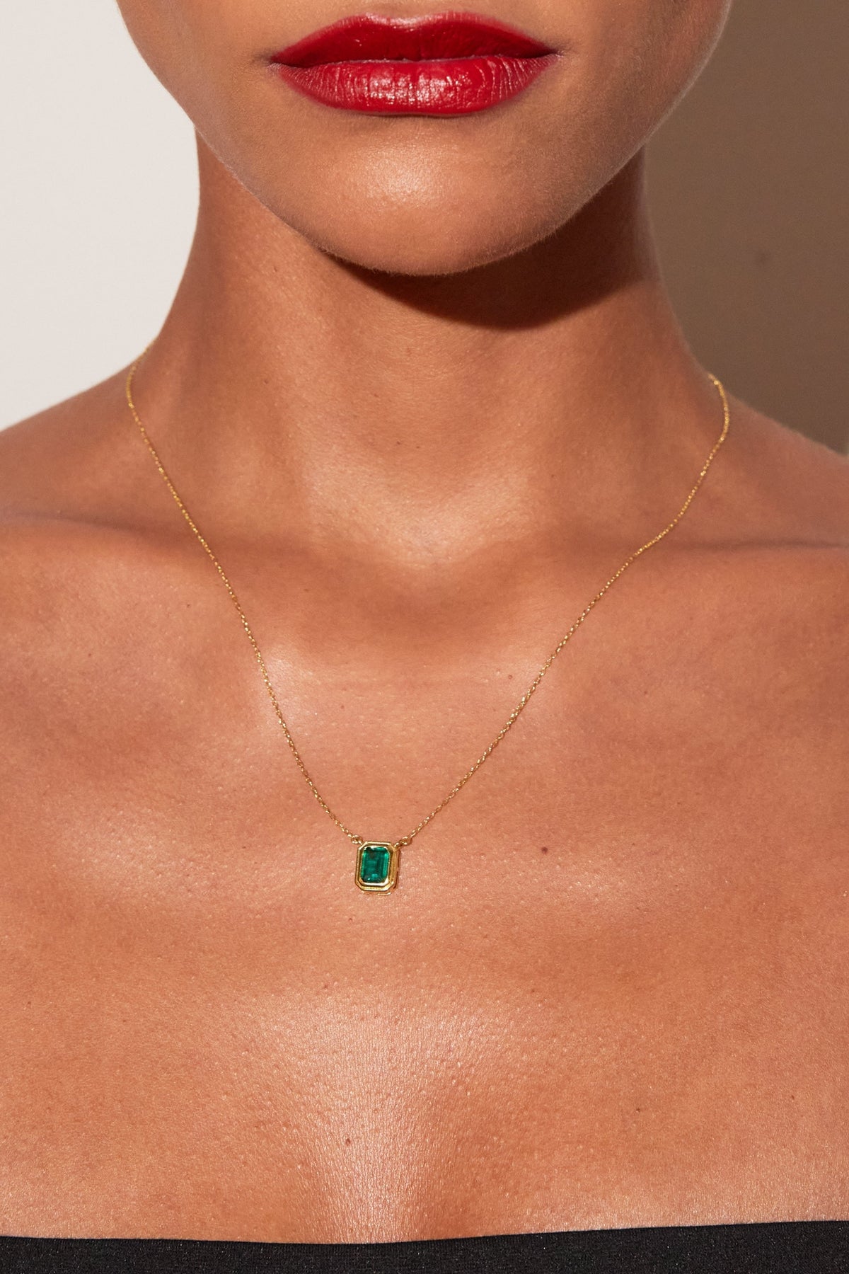 Close-up of a necklace with a green gemstone on a person's neck against a neutral background