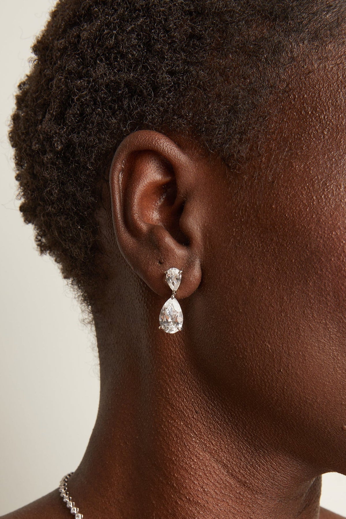 Close-up of a person wearing a silver teardrop earring against a neutral background