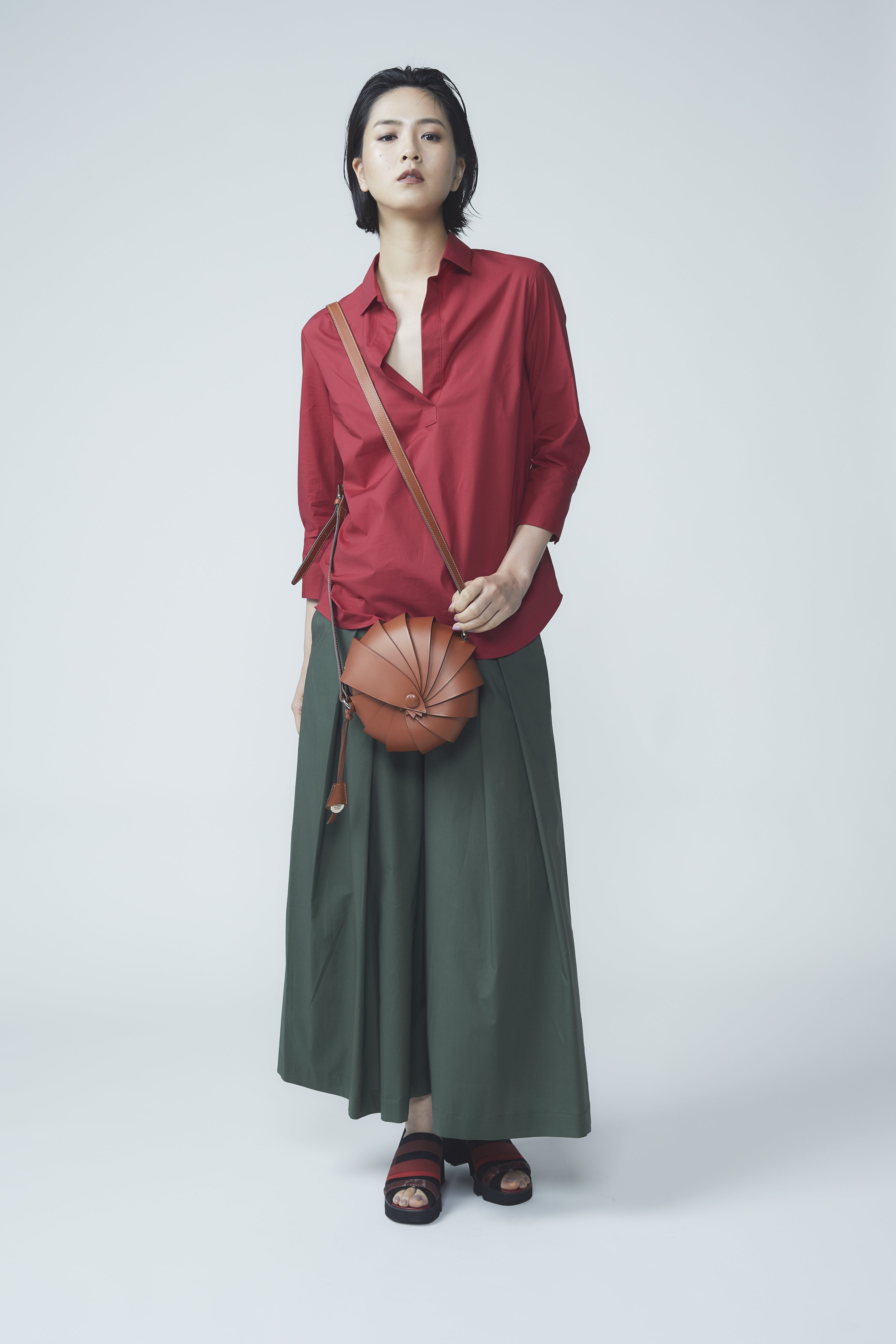 Woman wearing a red blouse and green skirt with a brown bag on a white background