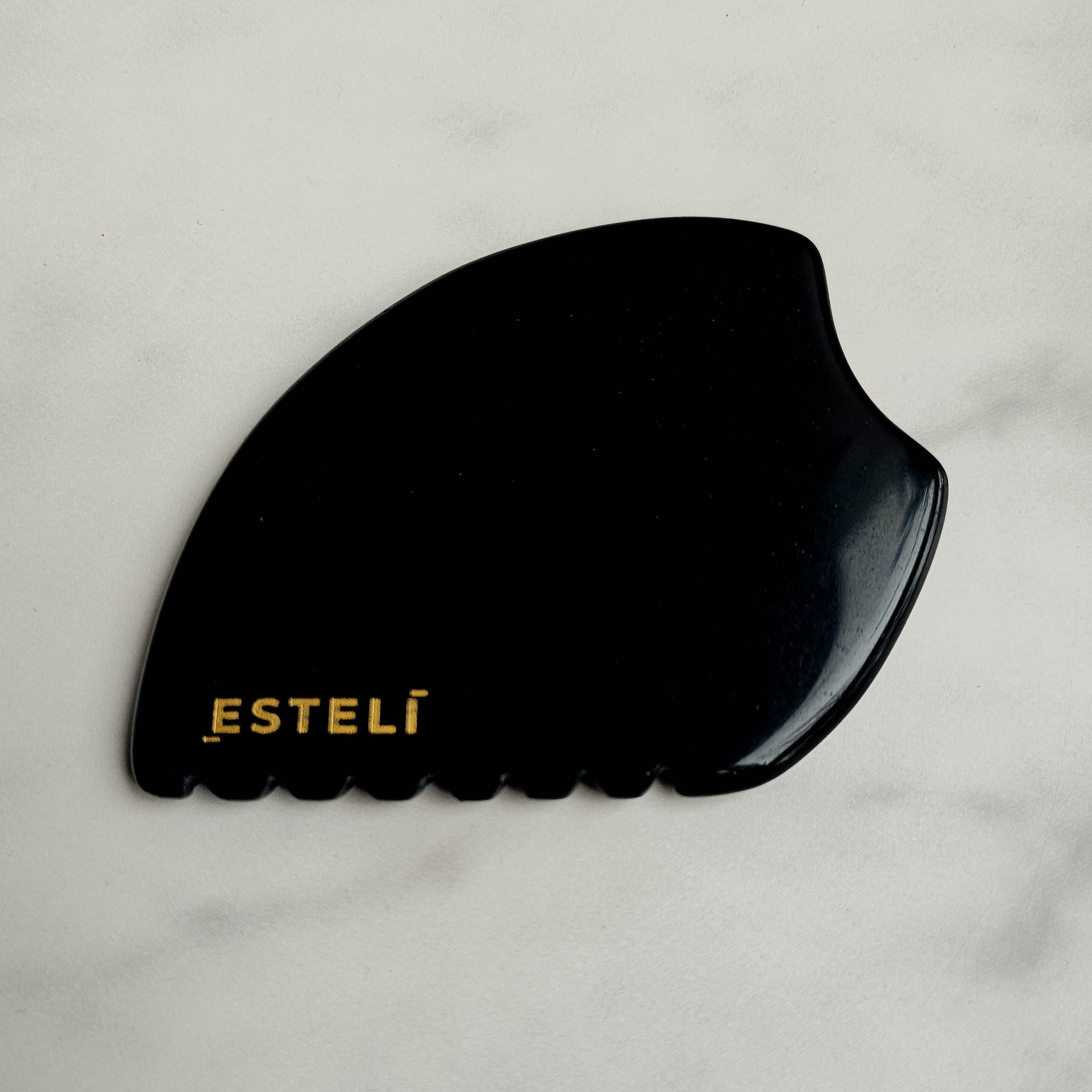 Black gua sha tool with 'ESTELI' branding on a light gray background