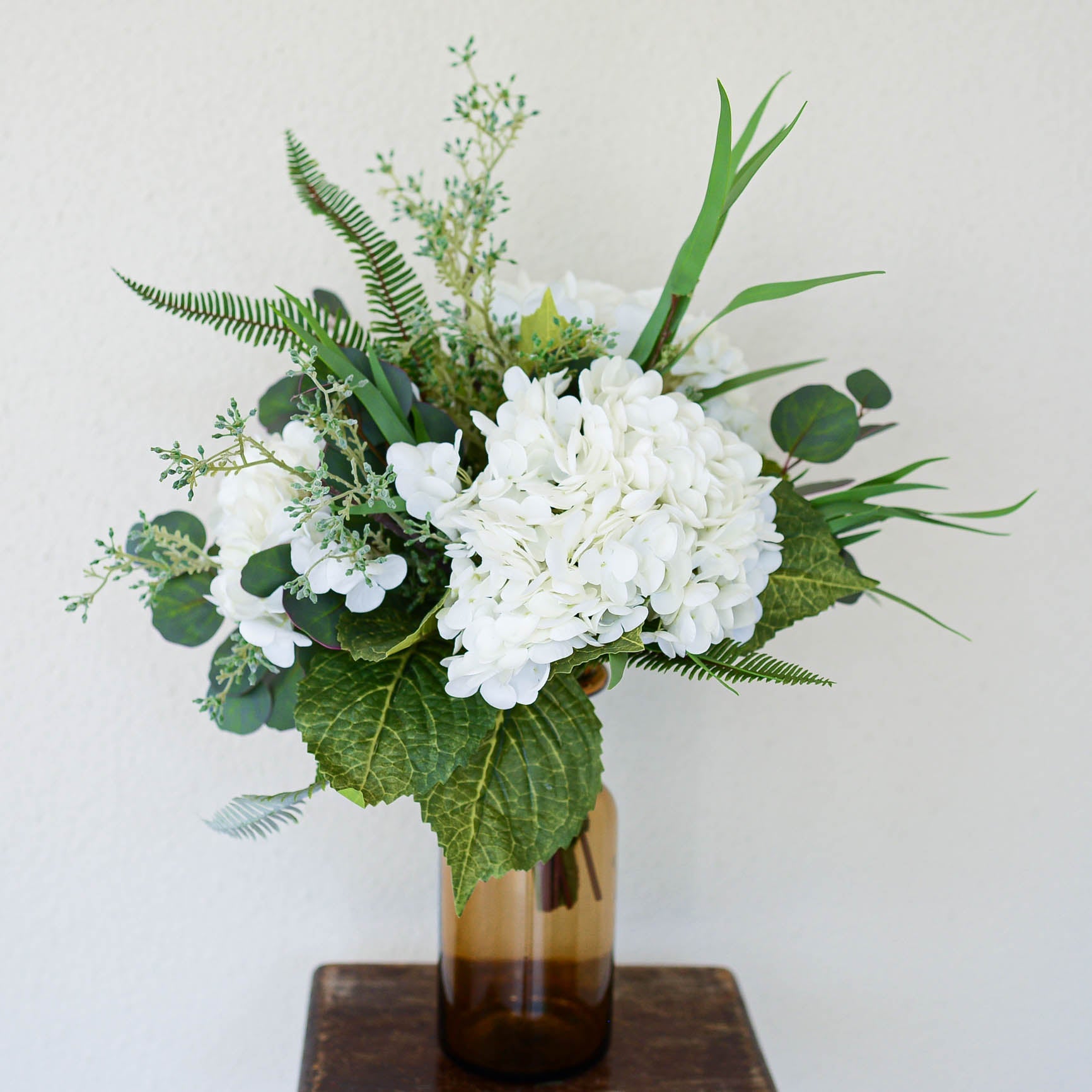 Bouquet of white flowers and greenery in a brown vase on a wooden surface with a light gray background