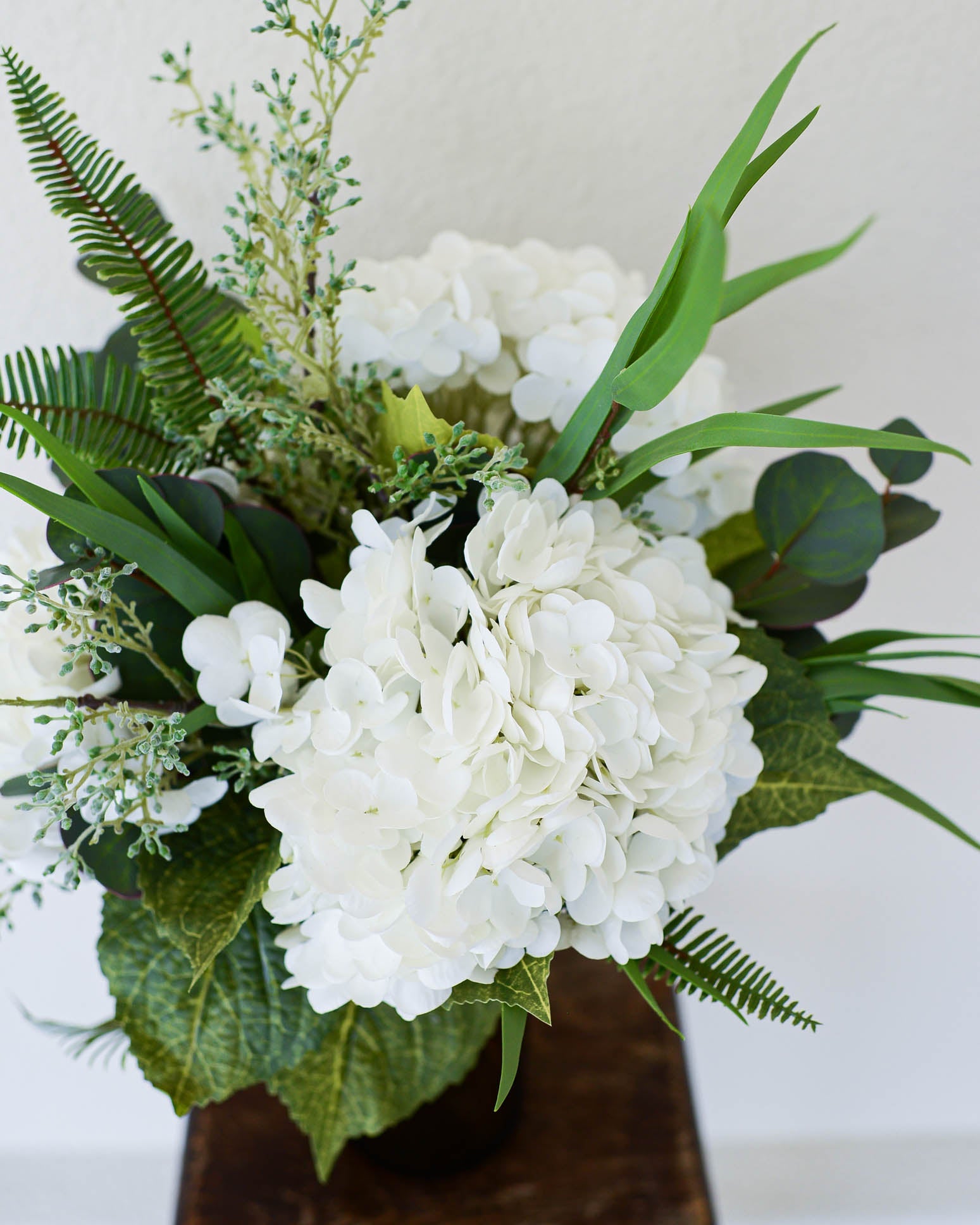 Floral arrangement with white flowers and green leaves on a neutral background