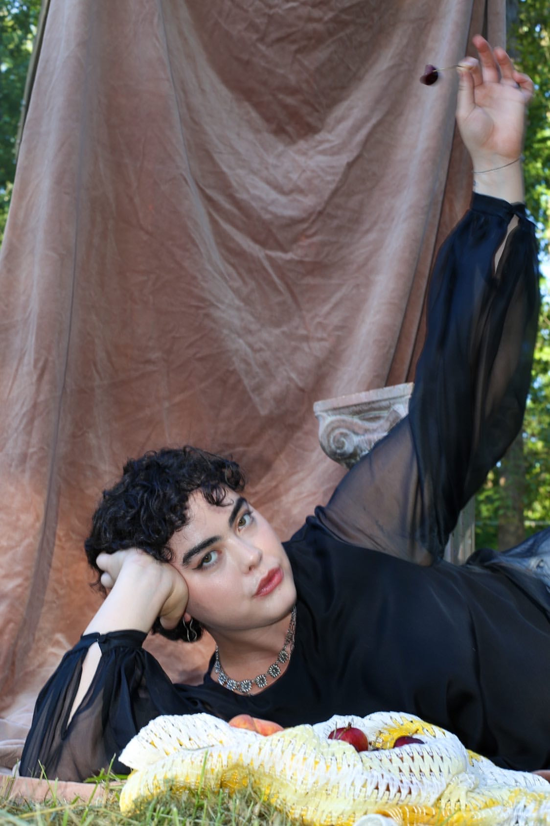 Person lying on grass with a large beige curtain and corn in the foreground