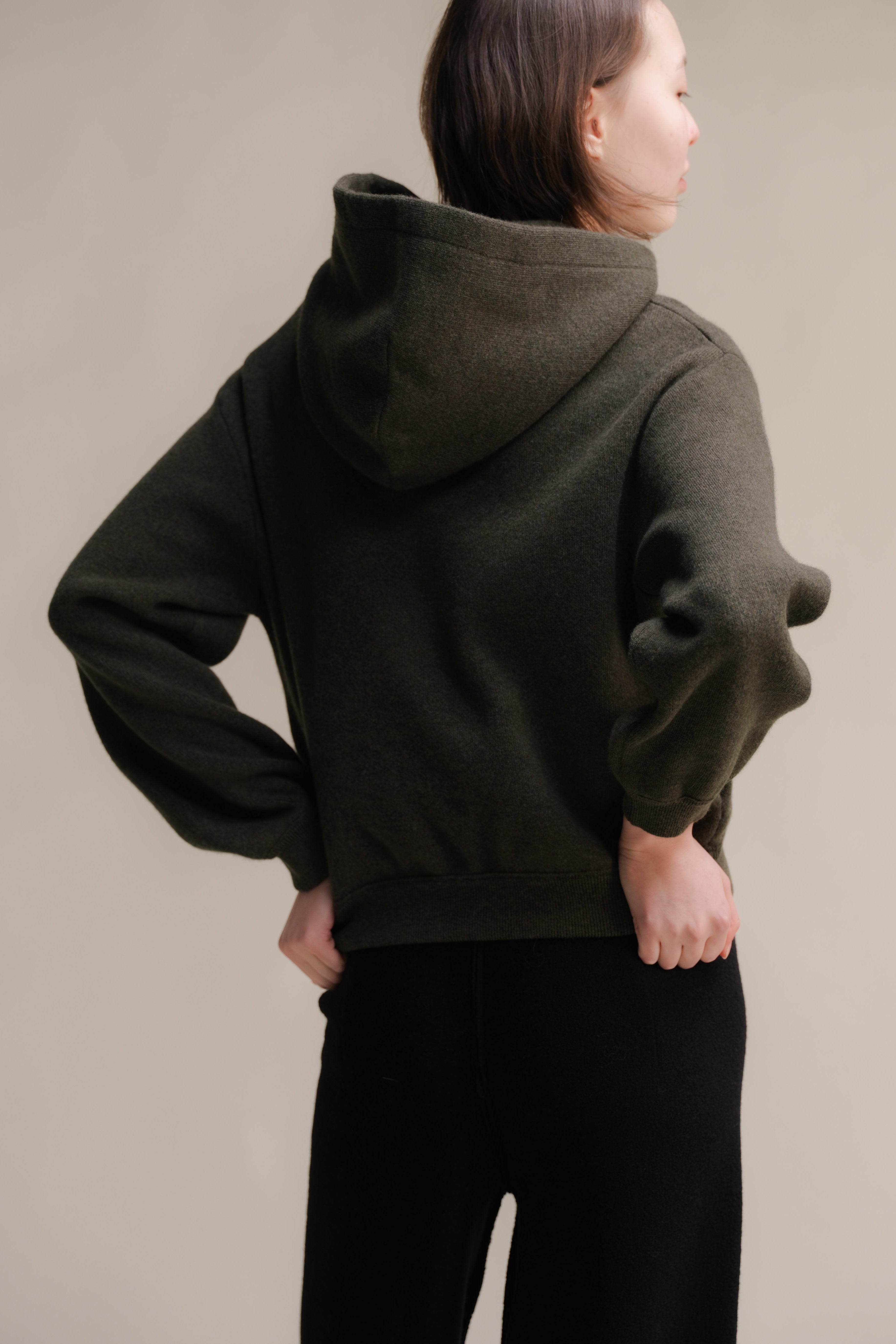 Person wearing a dark green hoodie with a neutral background