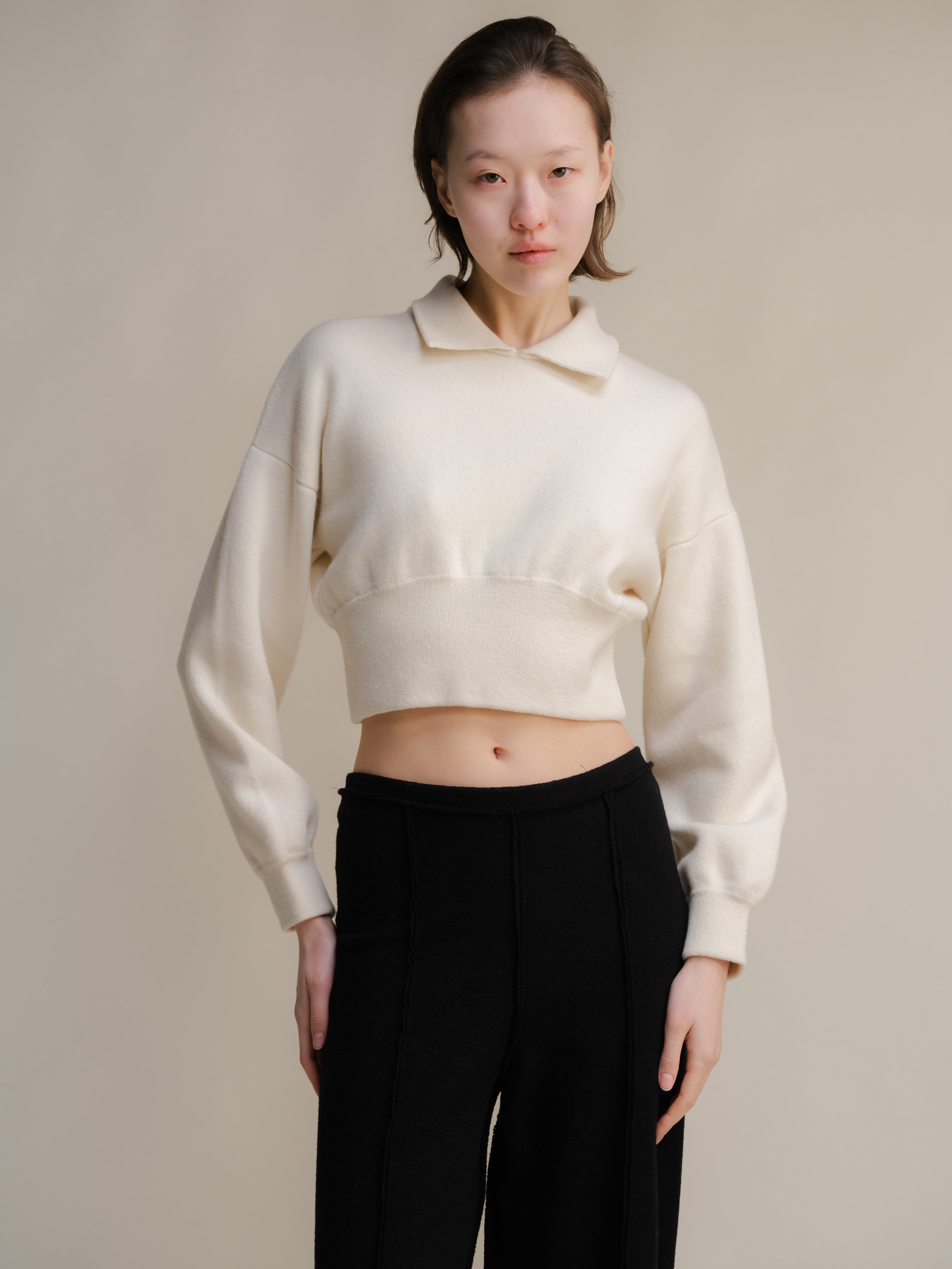 Person wearing a white cropped sweater and black pants against a plain background