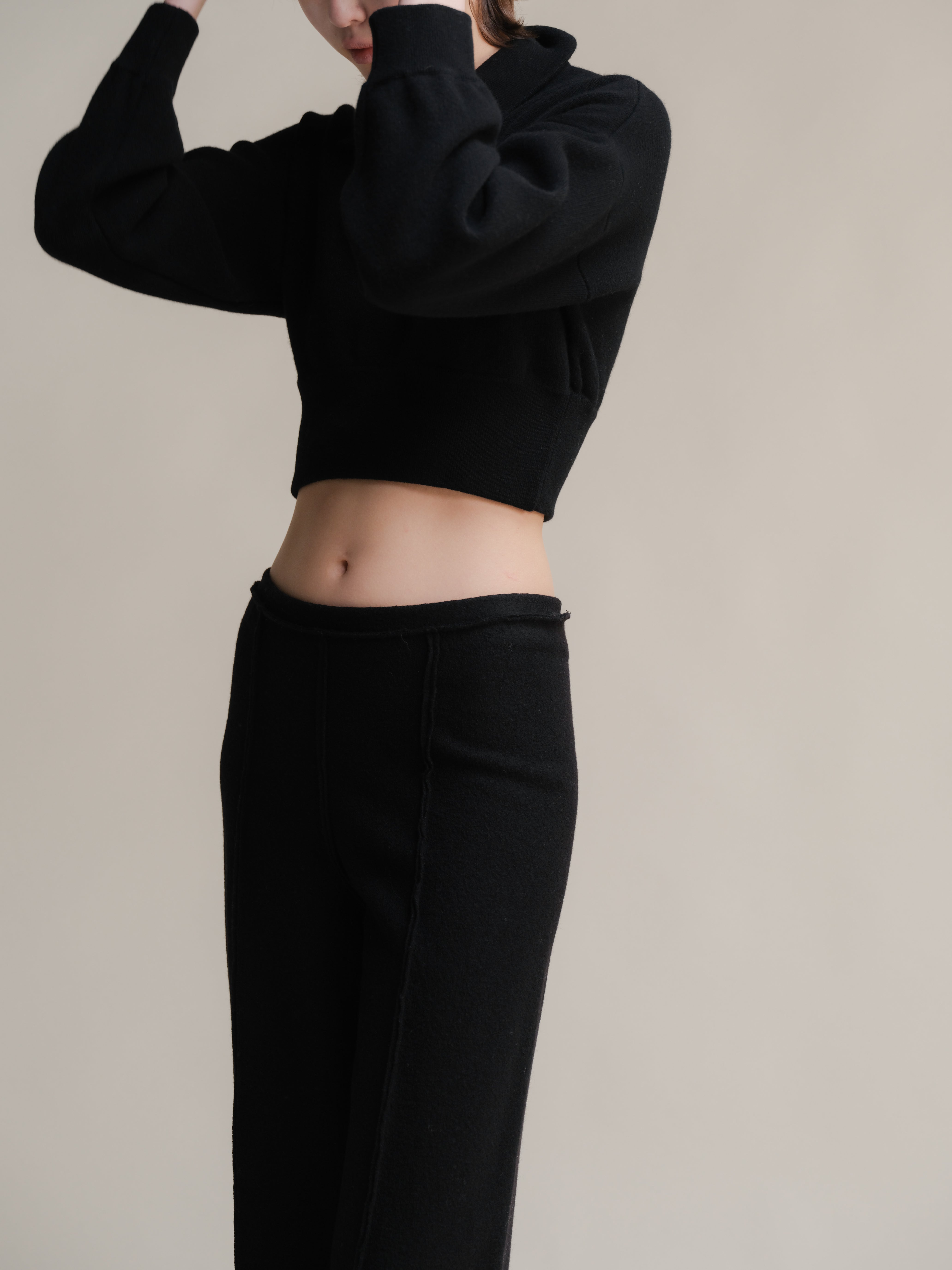 Person wearing a black cropped hoodie and black pants against a neutral background